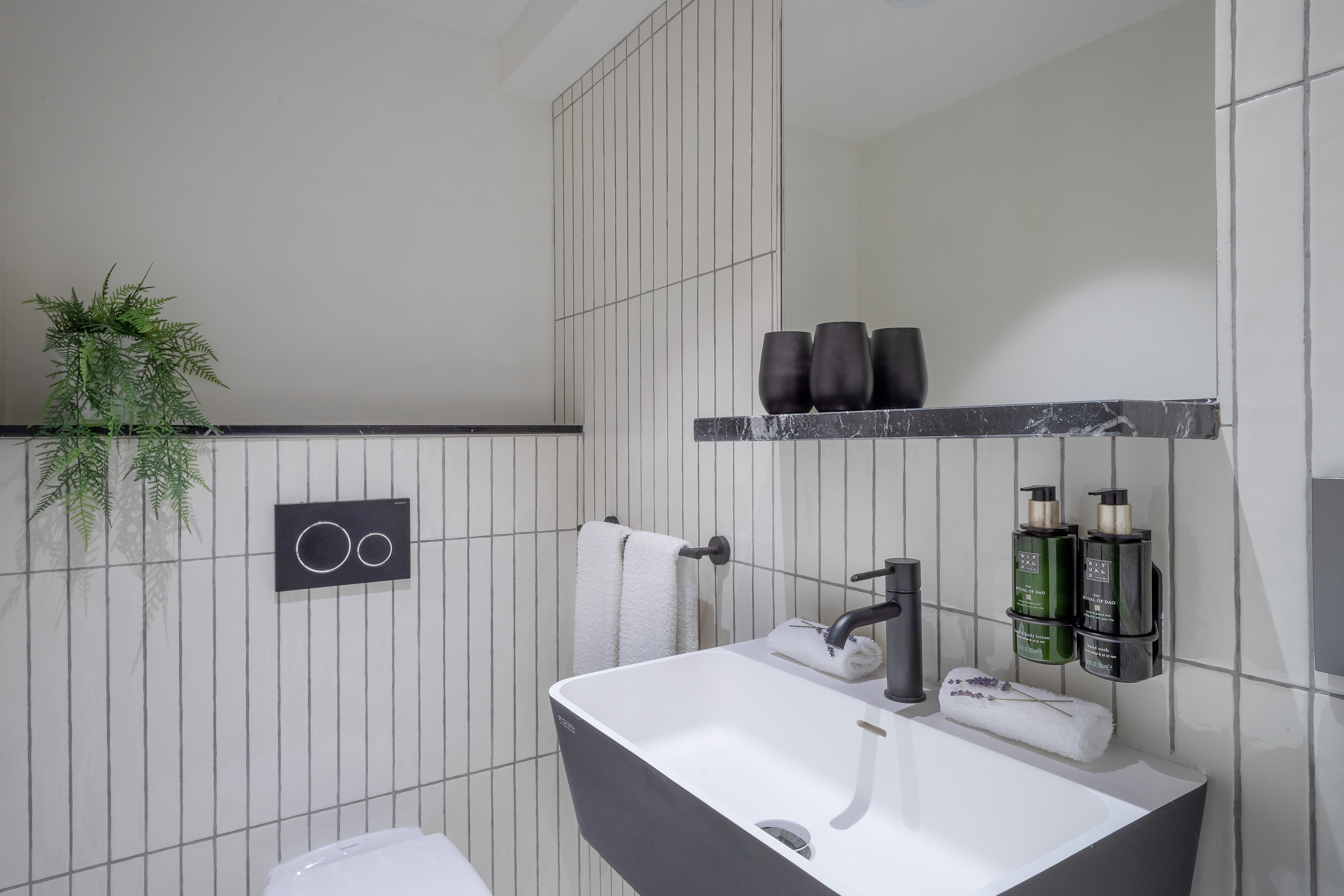 Modern bathroom with vertical white tiles, black sink, faucet, and toilet.
