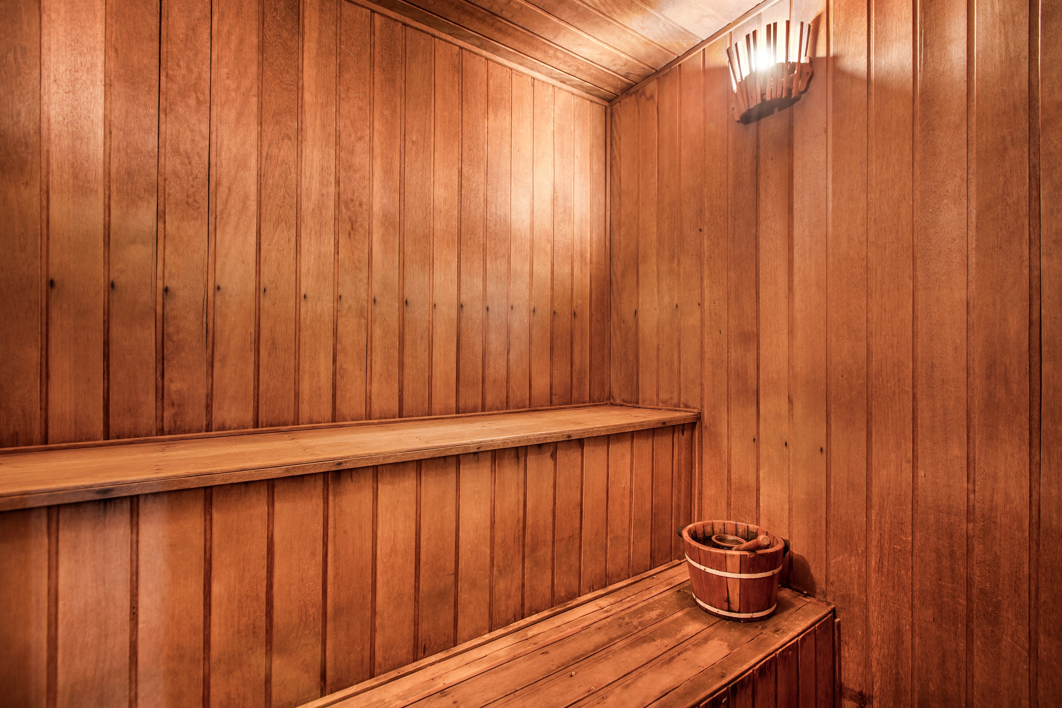 Wooden sauna interior with benches, bucket, and wall light.