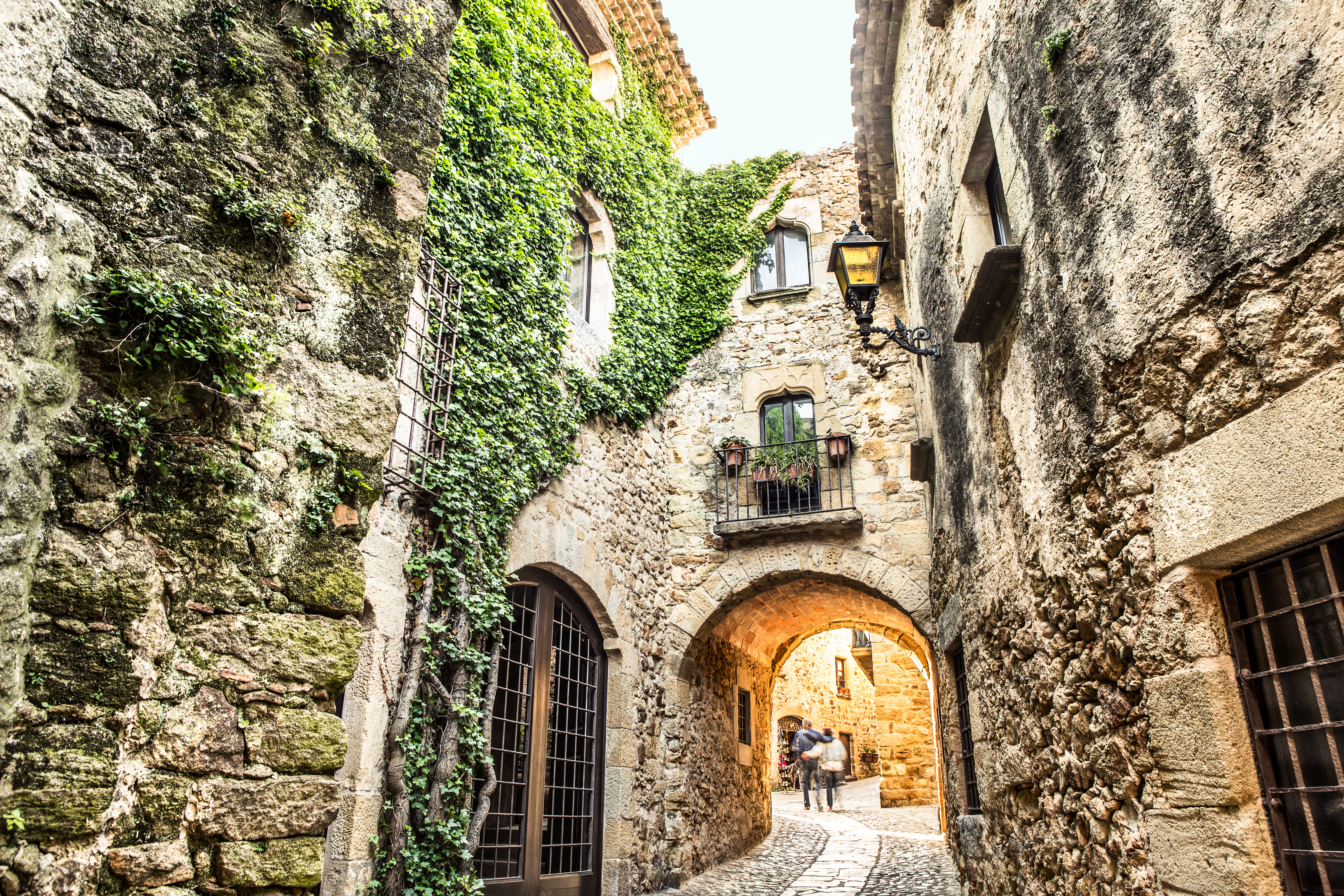 Callejón empedrado medieval con paredes de piedra, hiedra y un arco.