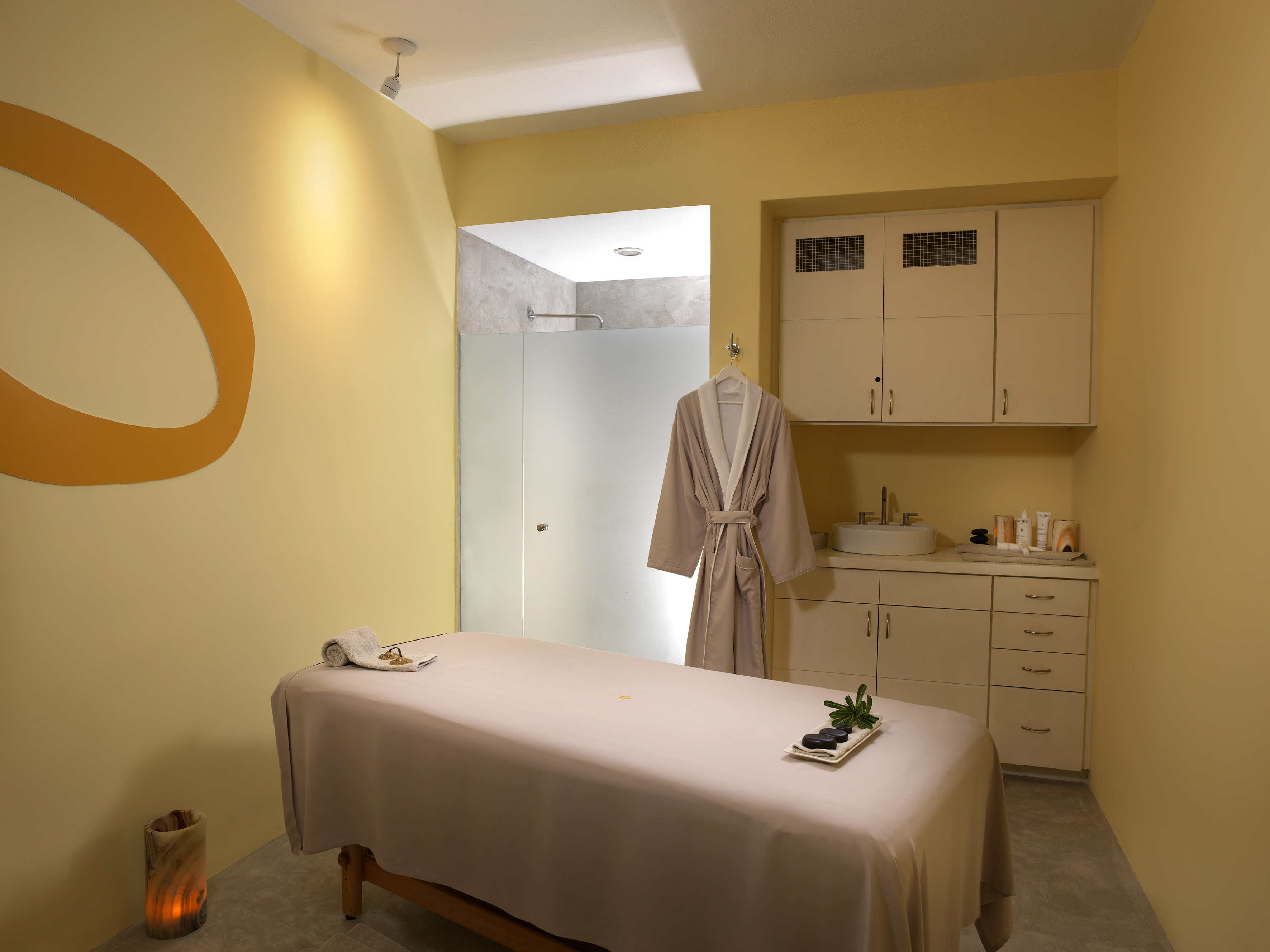 Spa massage room with treatment table, hot stones, bathrobe, and shower.