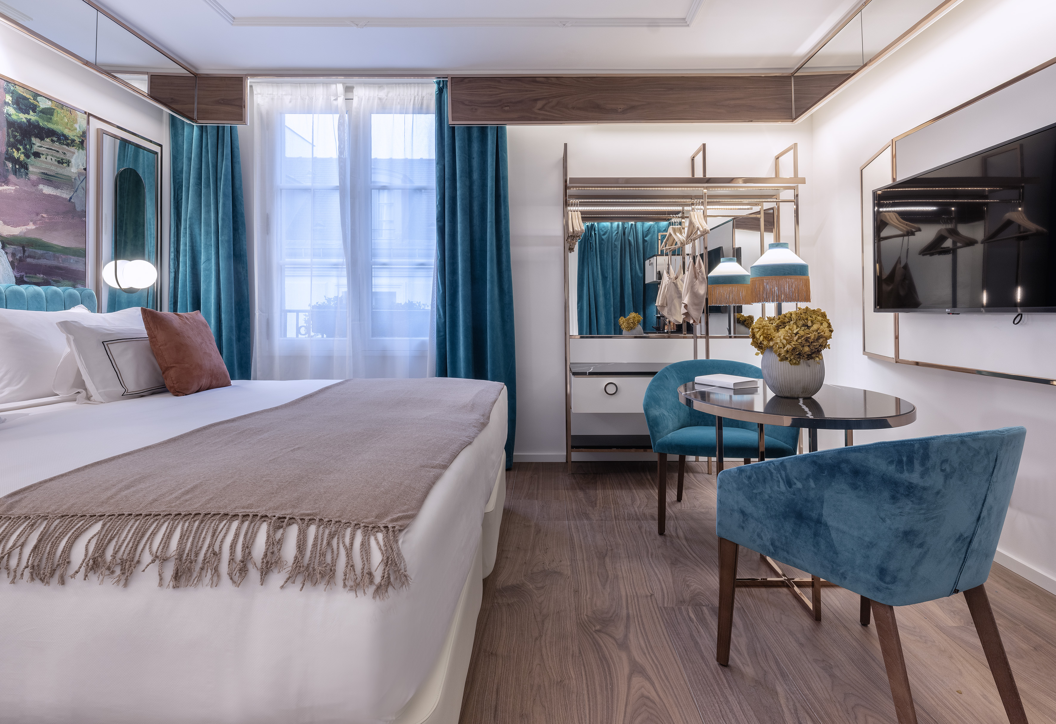 Modern hotel bedroom with white bed, teal accents, wood floor, and seating area.
