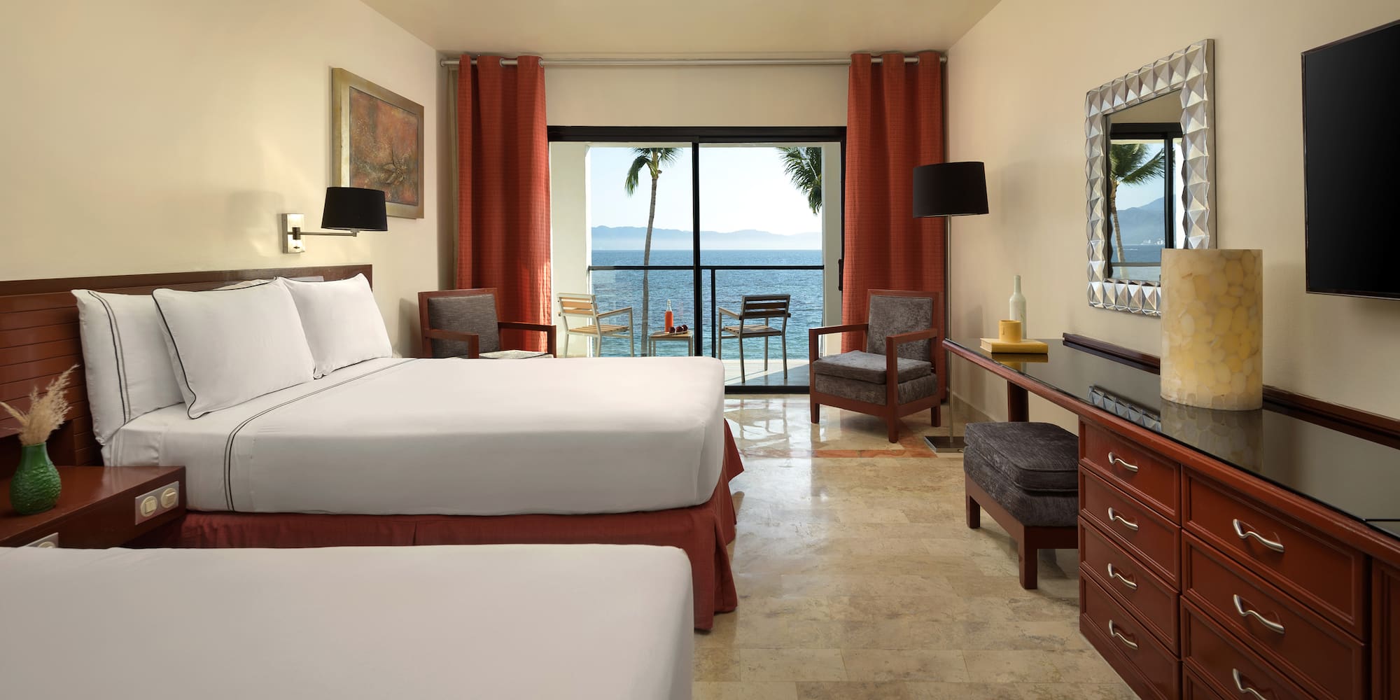 a room with a bed and chairs and a table with a view of the ocean