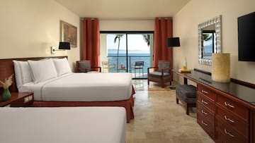 a room with a bed and chairs and a table with a view of the ocean