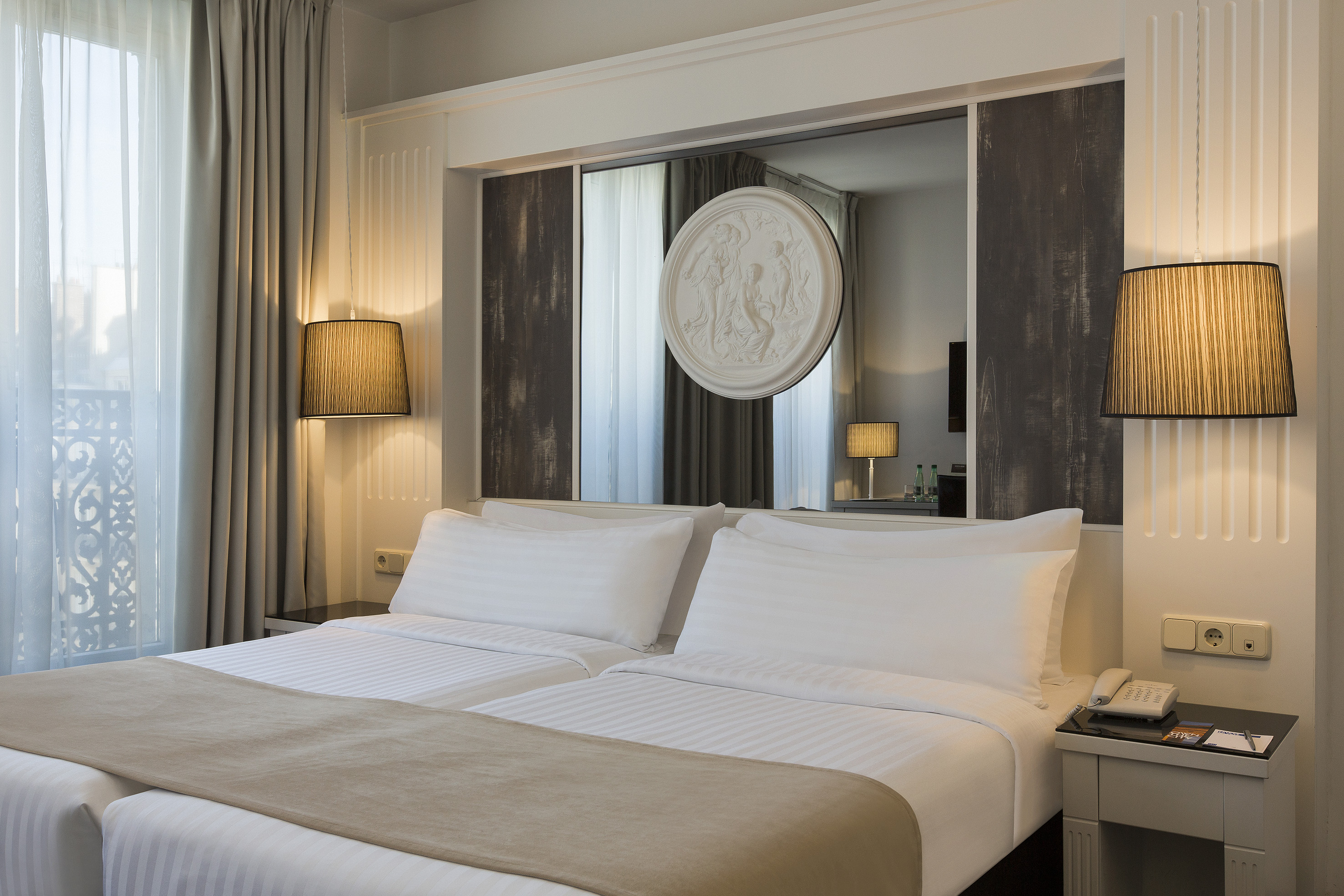 Modern hotel bedroom with twin beds, lamps, and decorative mirrored headboard.