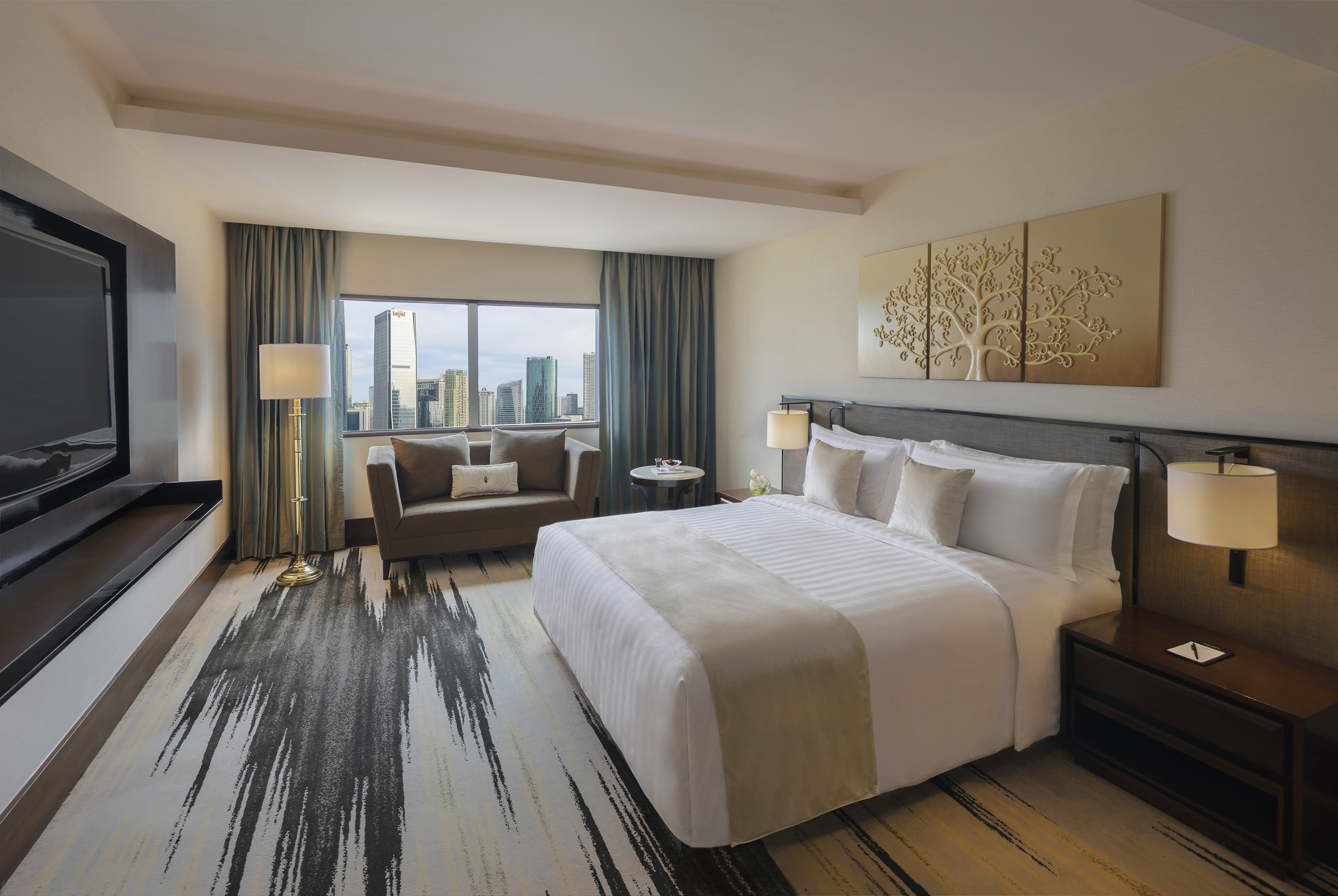 Modern hotel suite with king bed, city skyline view, sofa, and elegant decor.