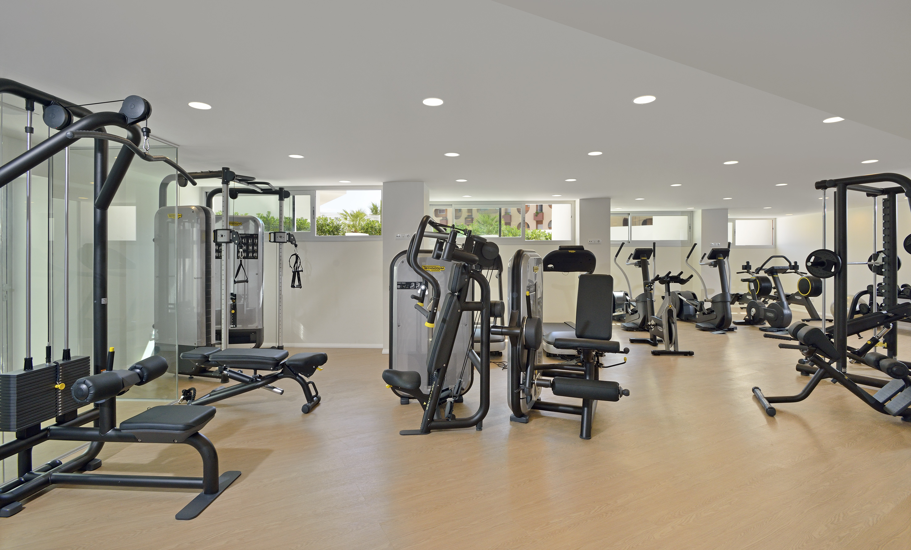 Modern gym with Technogym weight machines, cardio equipment, and bright windows.