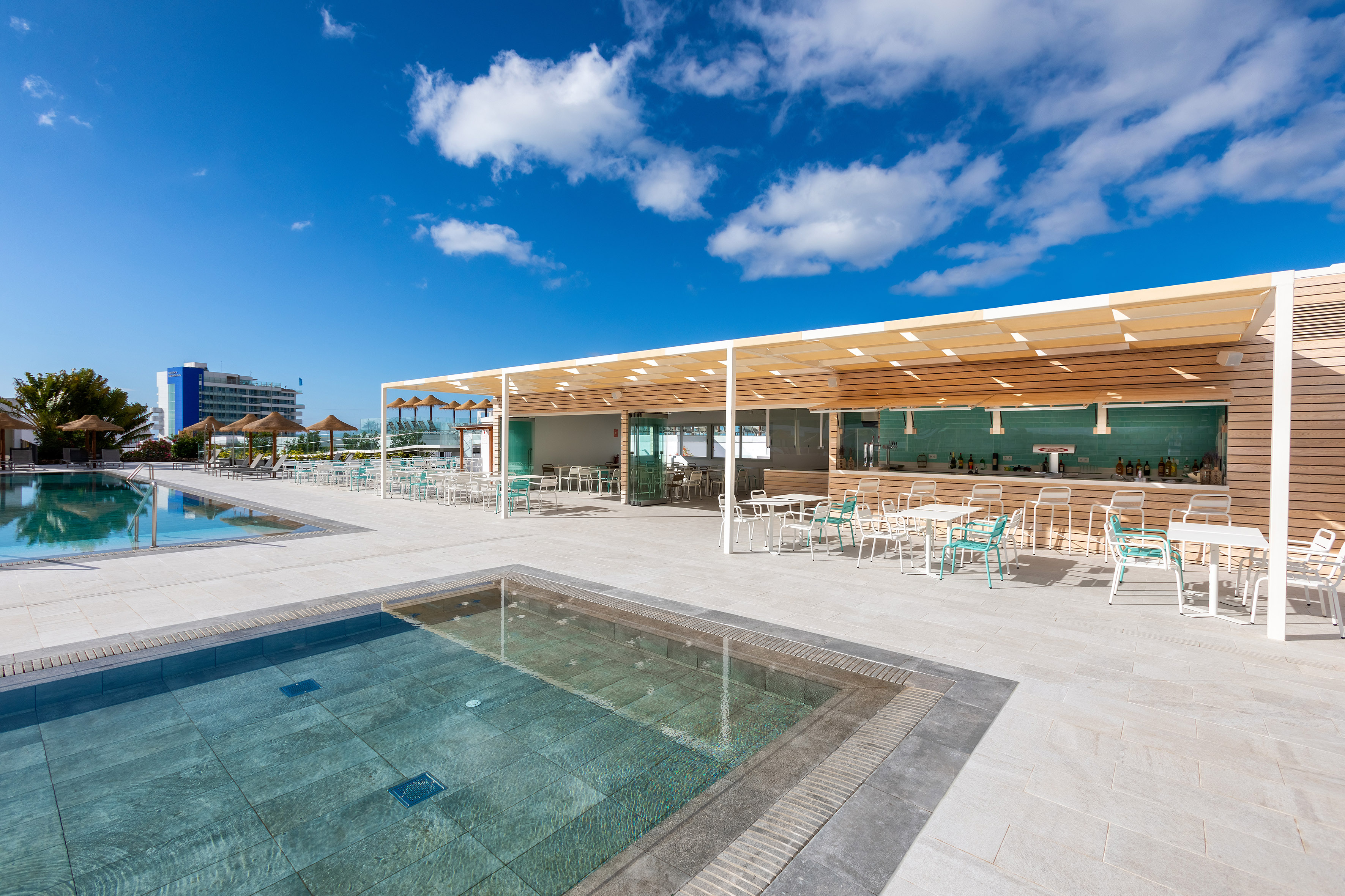 Hotel poolside bar with modern design, outdoor seating, and two clear blue pools.