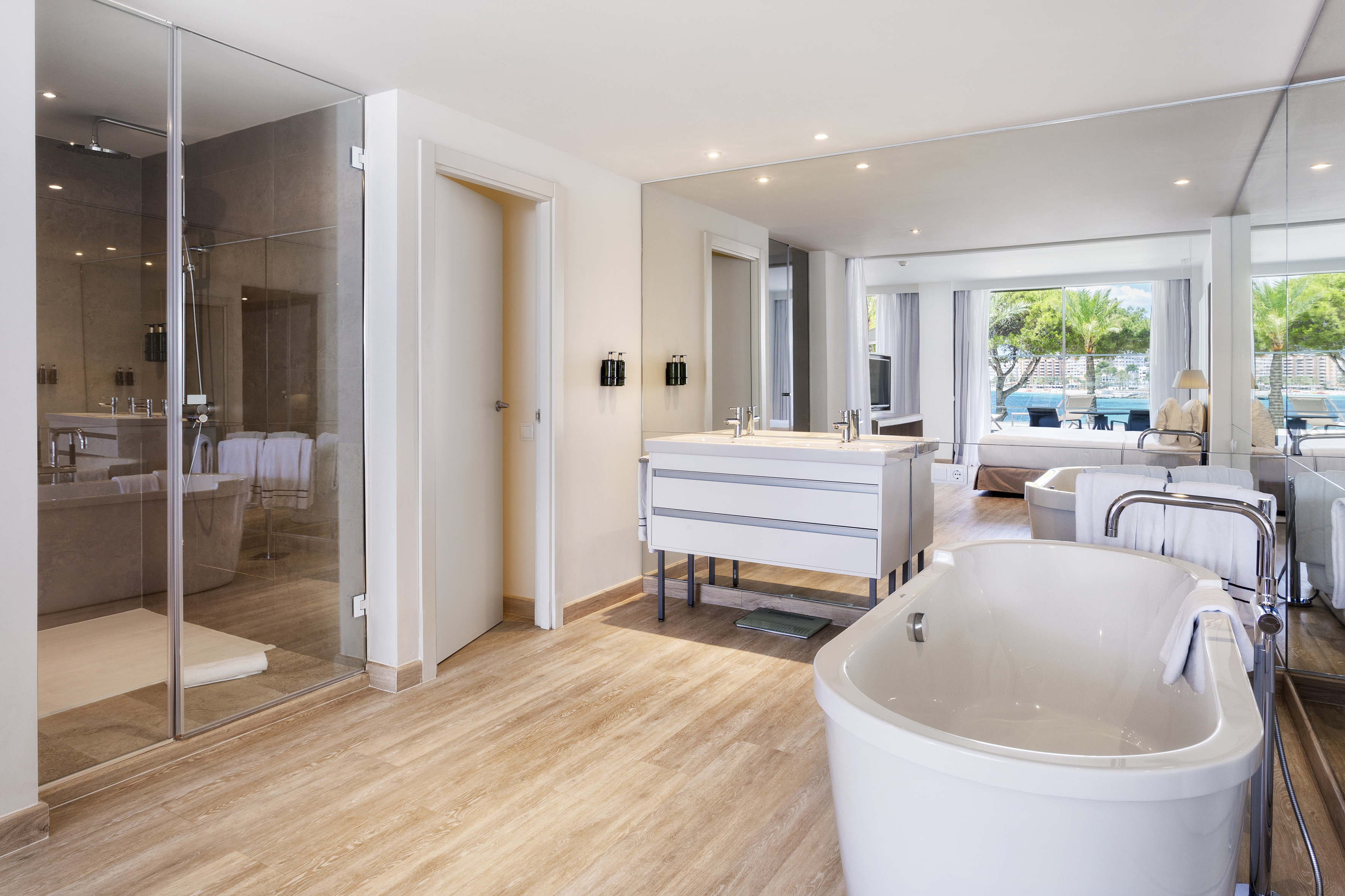 Spacious hotel bathroom with freestanding tub, walk-in shower, and sea view.