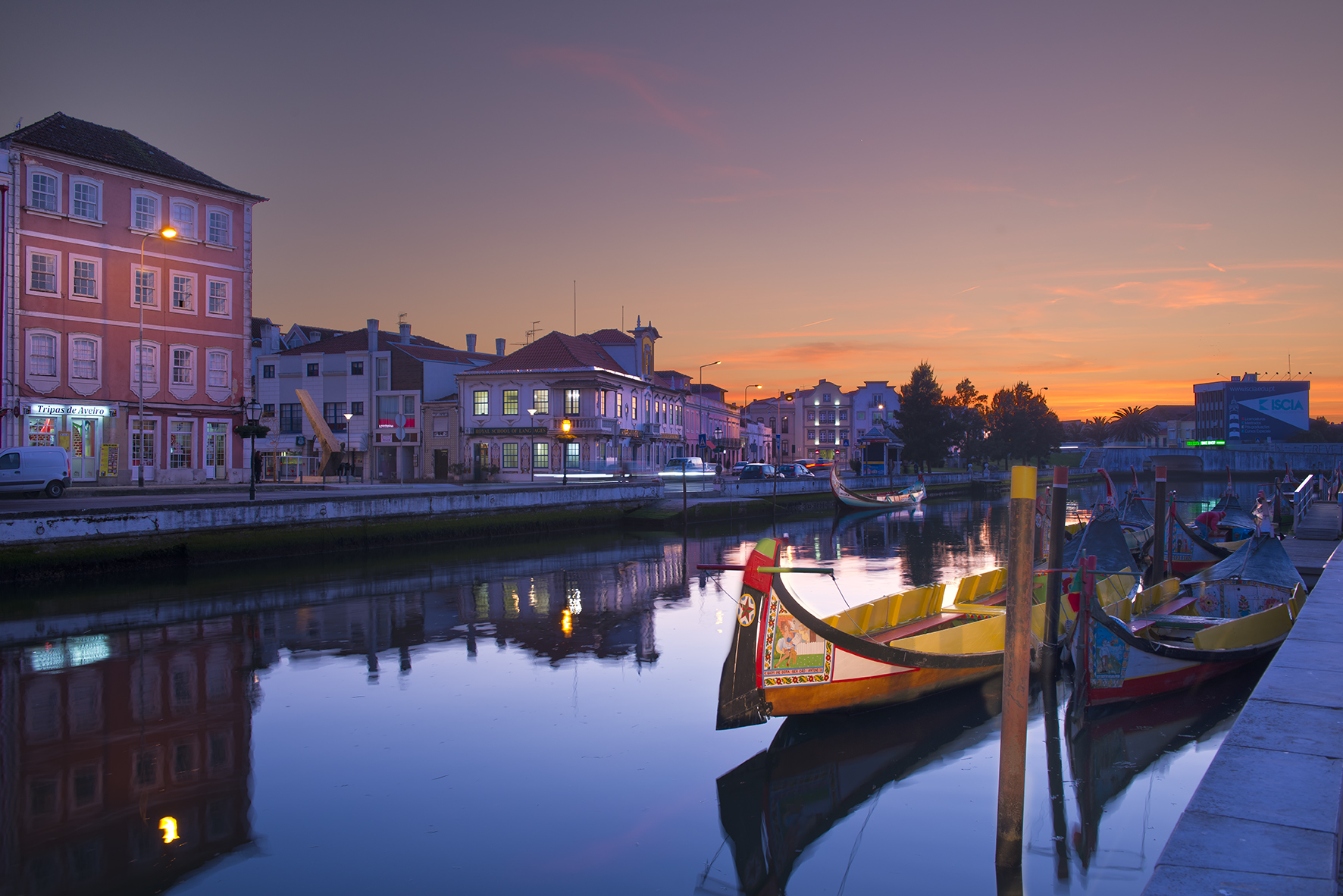 Moliceiro boats in Aveiro canal at dusk with illuminated buildings and reflections.