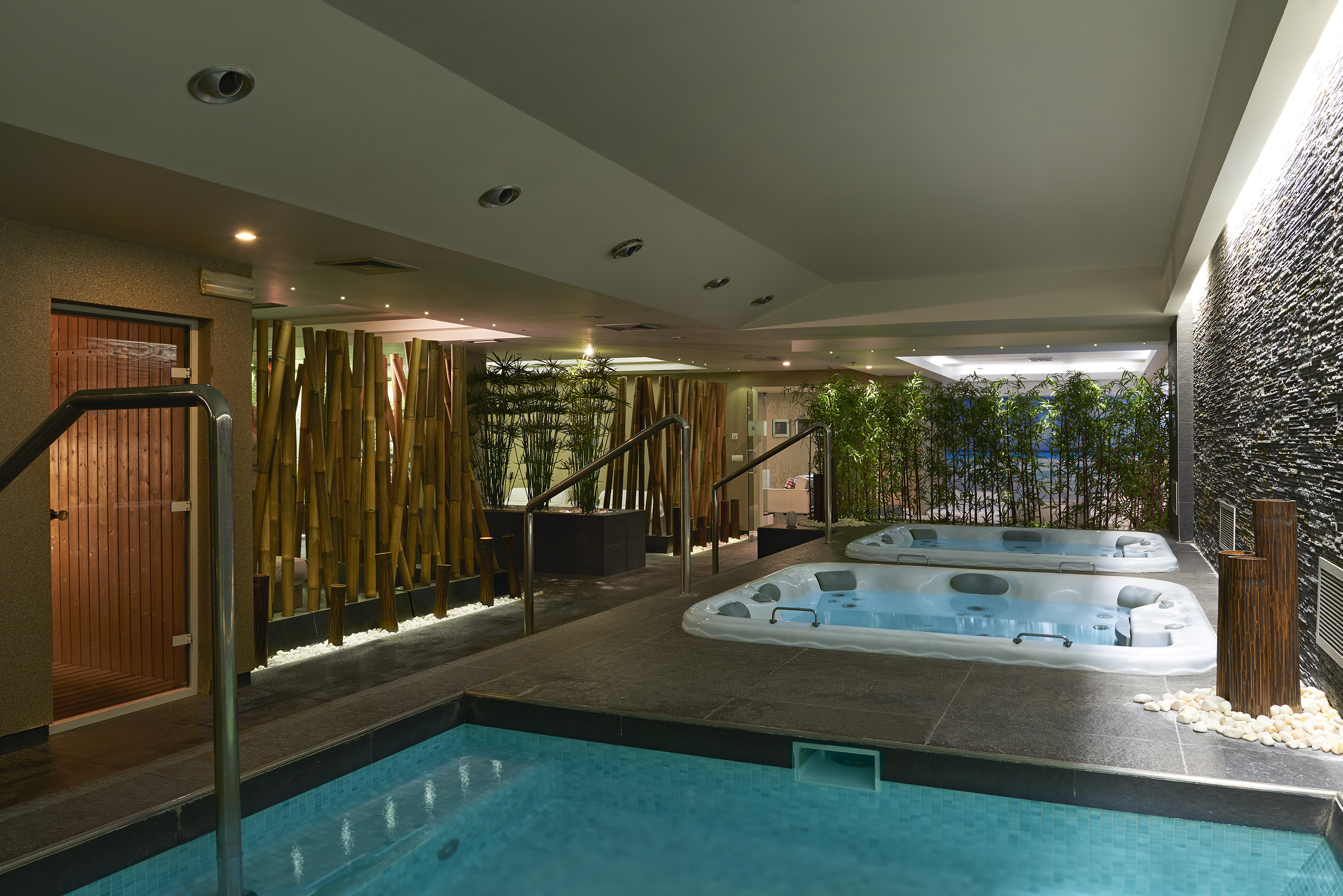 Indoor wellness spa with two jacuzzis, swimming pool, and bamboo accents.