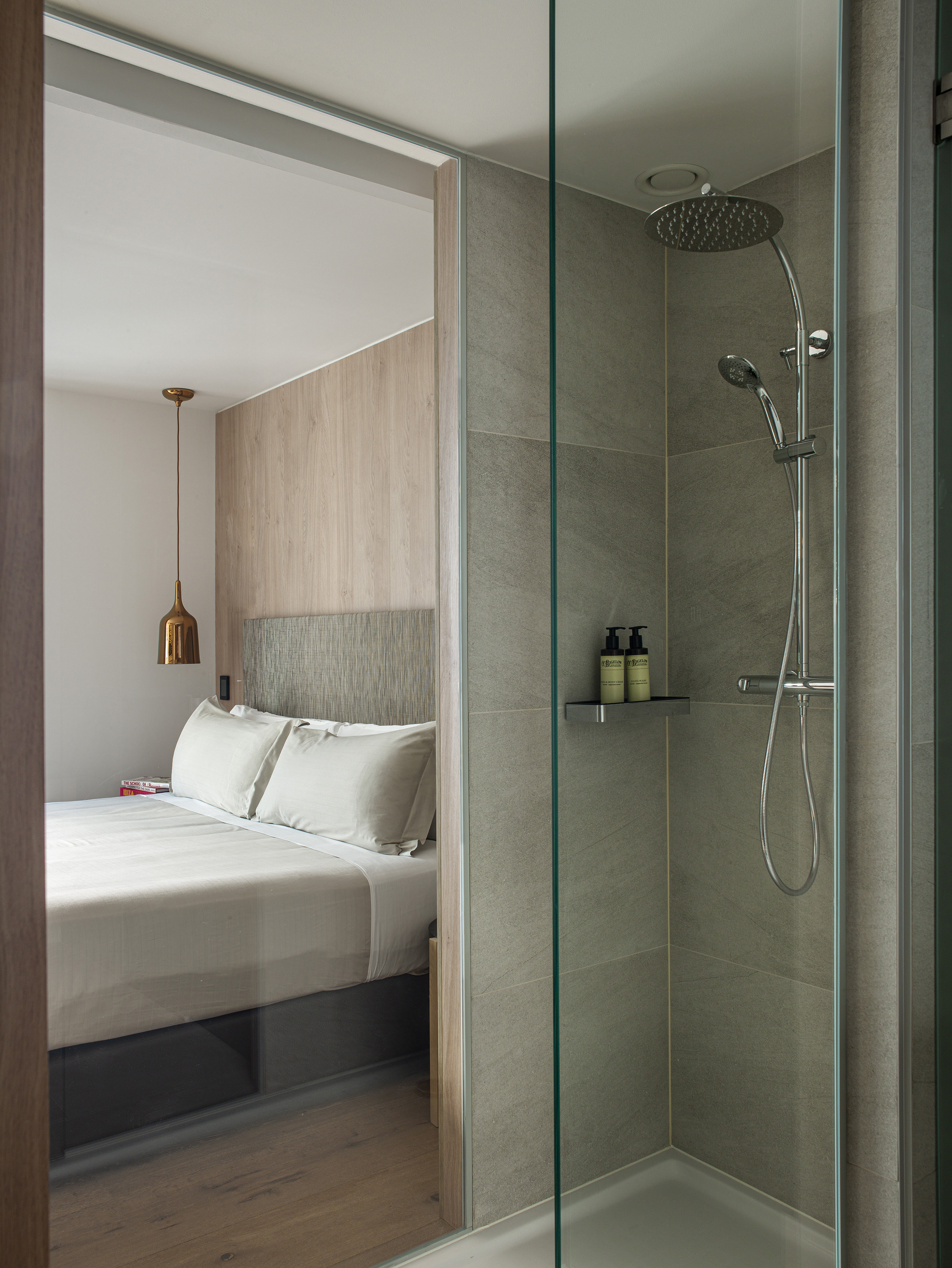 Modern hotel room showing bed and glass-enclosed shower with grey tiles.