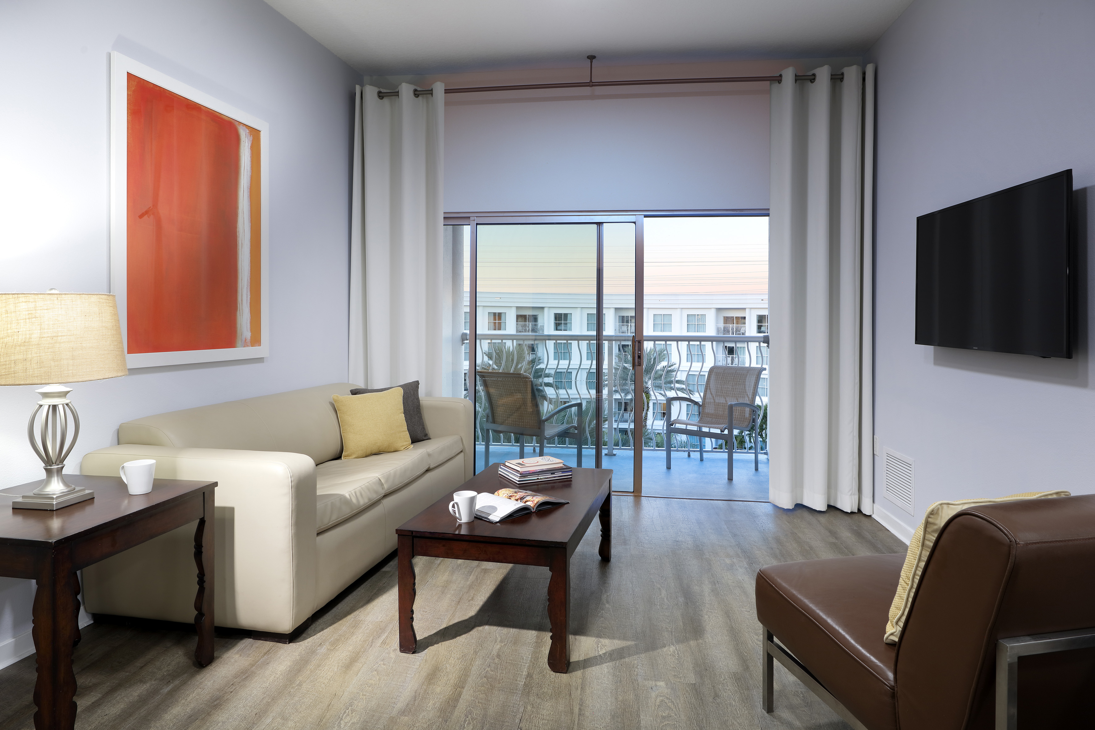 Hotel suite living room with beige sofa, flat-screen TV, and balcony. - Two-Bedroom Family Suite - Meliá Orlando Celebration, Orlando