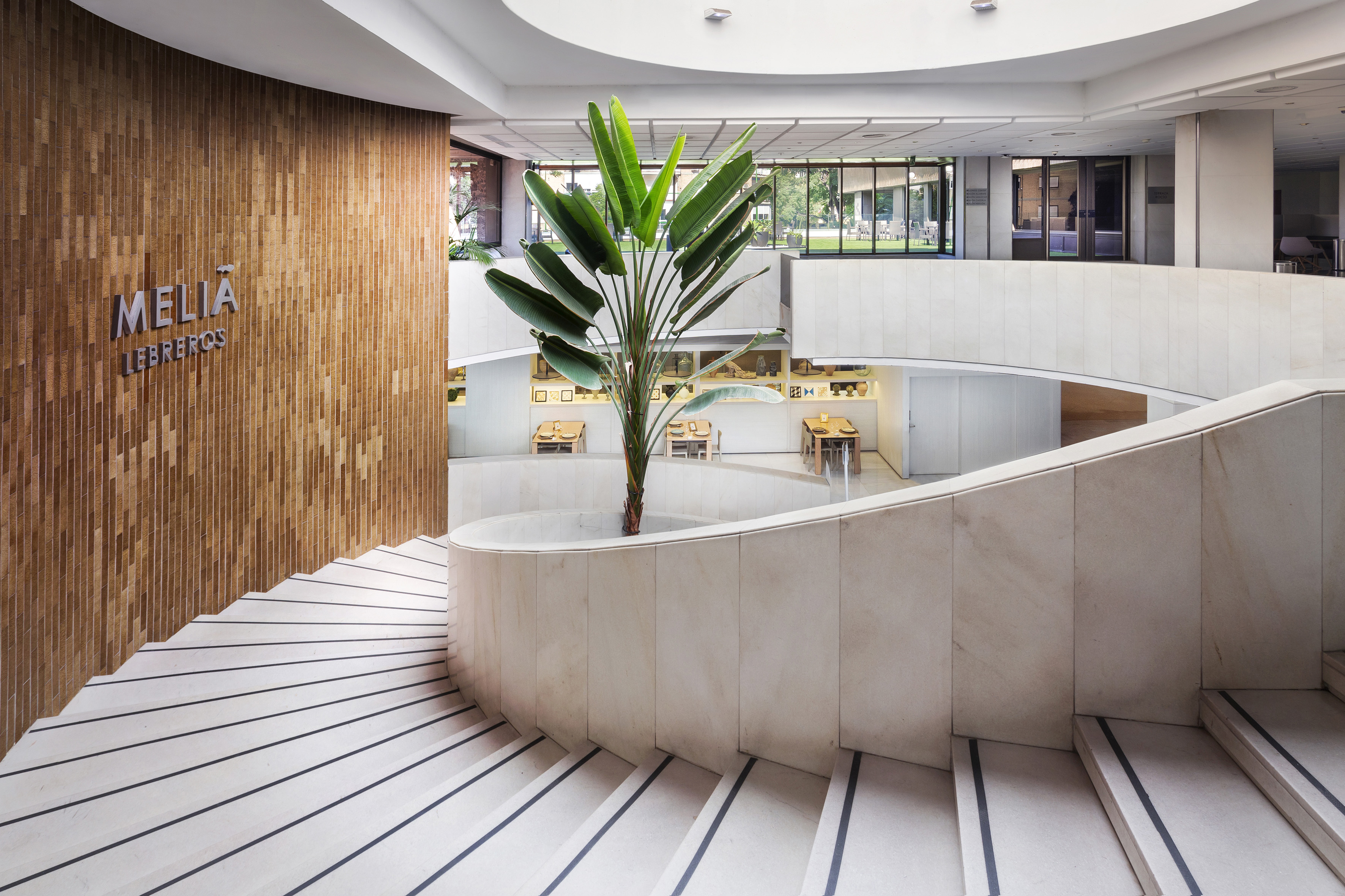Modern Meliá Lebreros hotel lobby with spiral staircase and large plant.