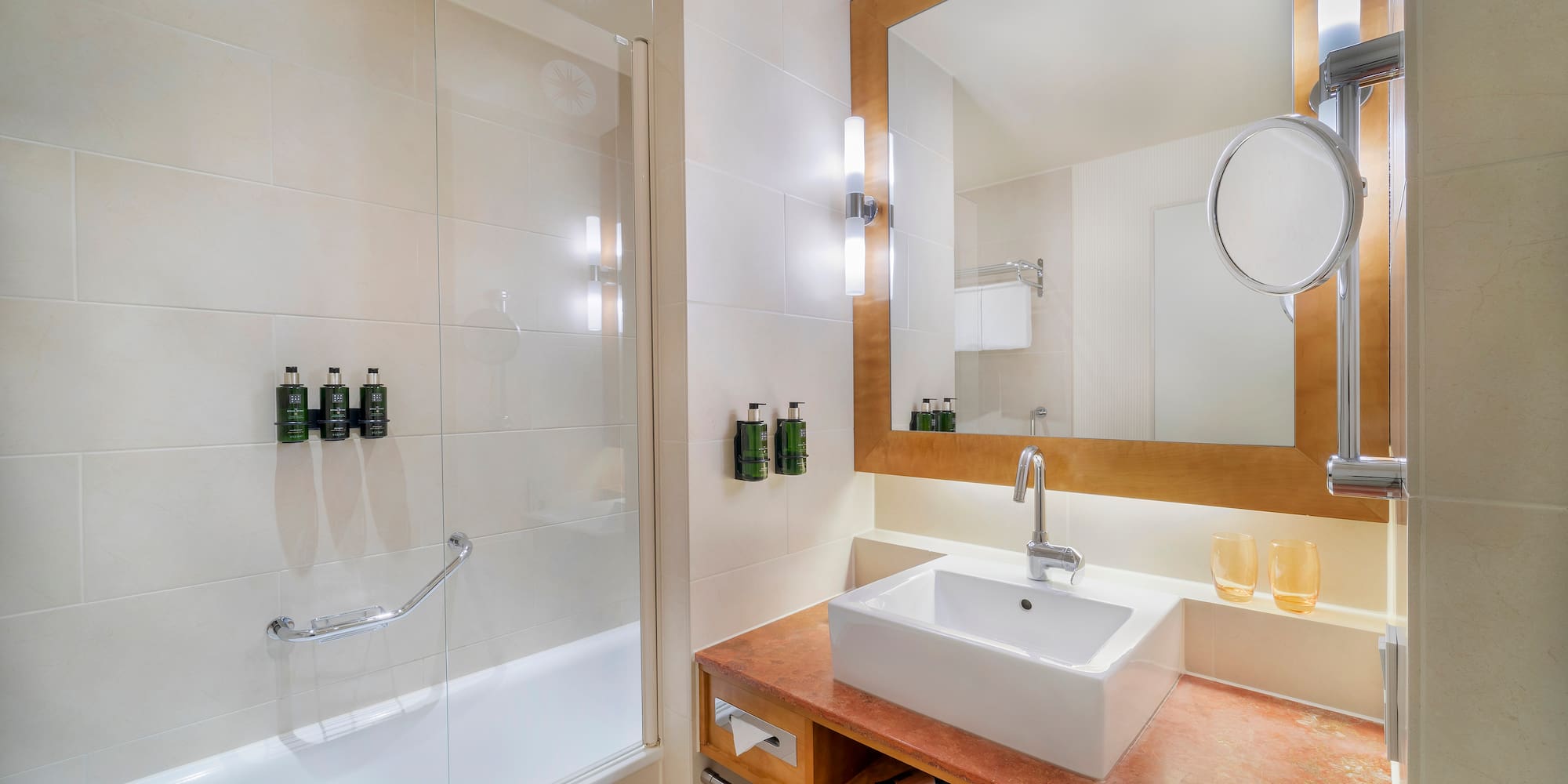 Modern hotel bathroom with white vanity, mirror, and glass shower tub.