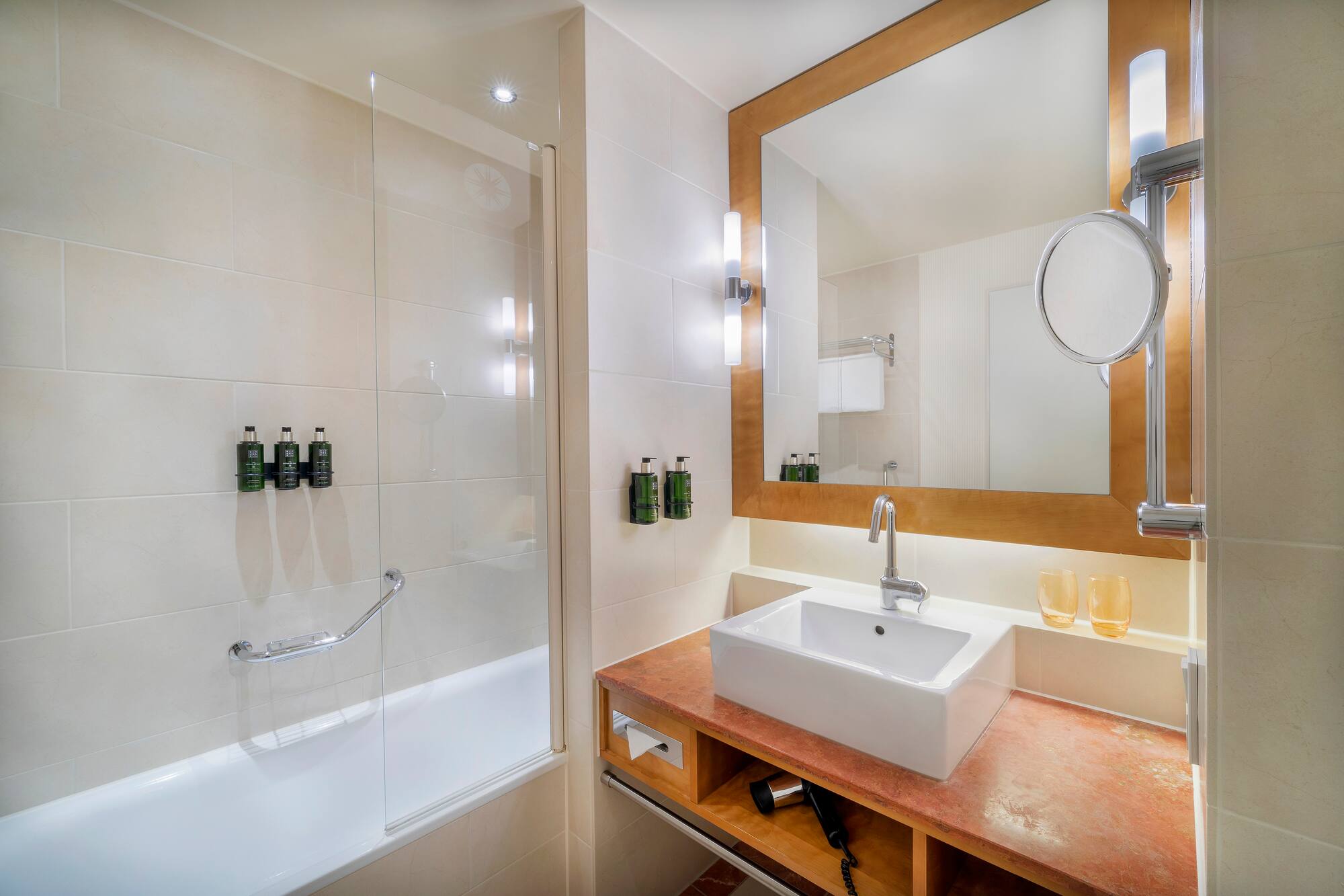 Contemporary hotel bathroom with white bathtub, vanity, large mirror, and amenities.