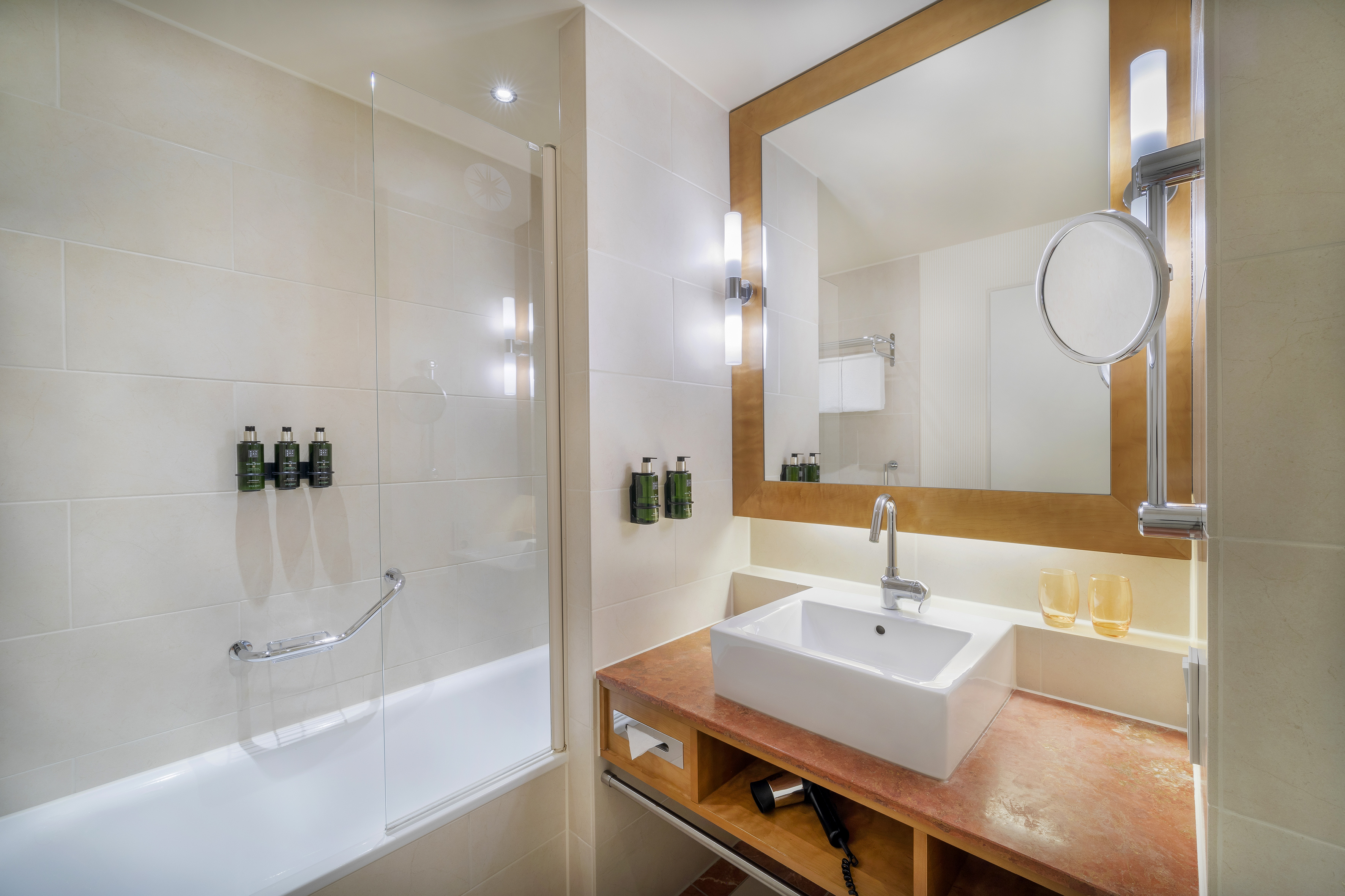 Modern hotel bathroom with white vanity, mirror, and glass shower tub.