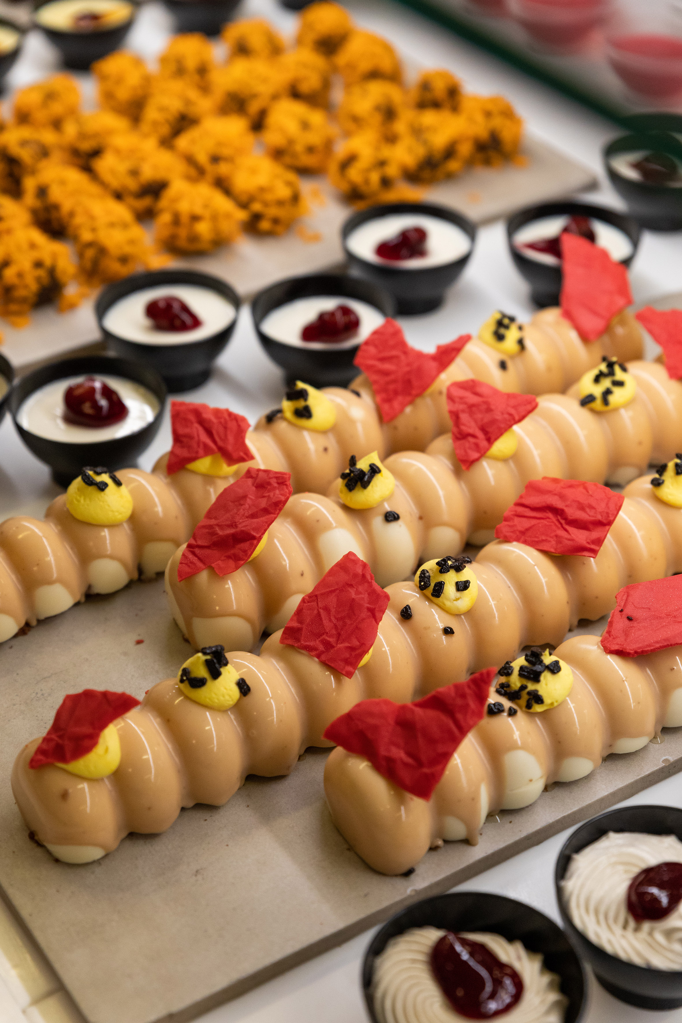 Caramel pastries with red/yellow accents, cream cups, and orange buffet desserts.