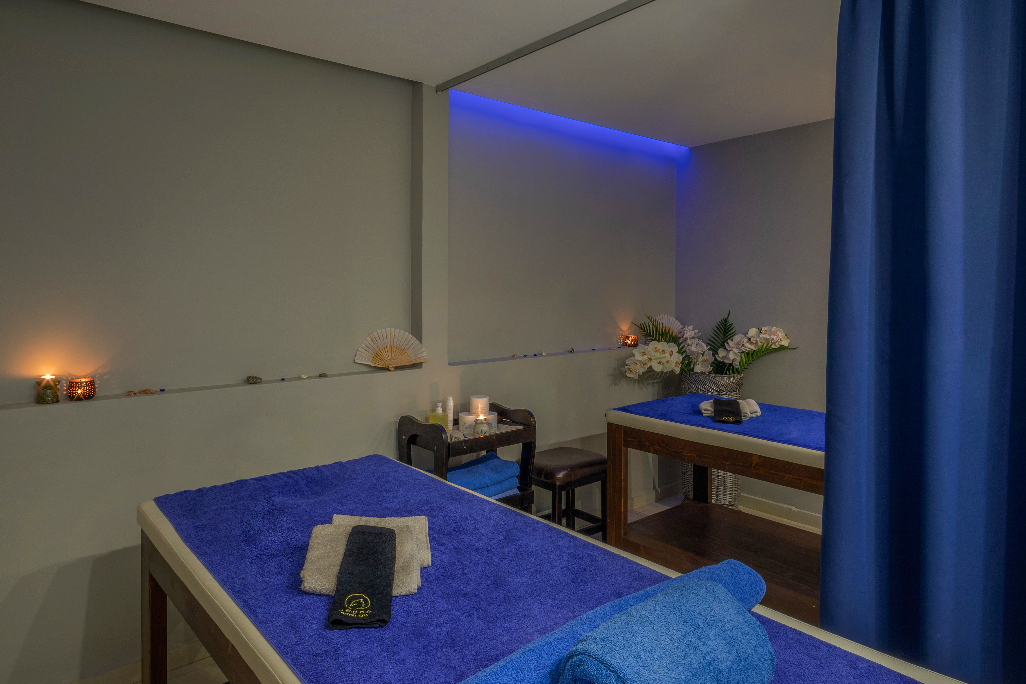 Relaxing spa massage room with two beds, blue towels, and ambient lighting.