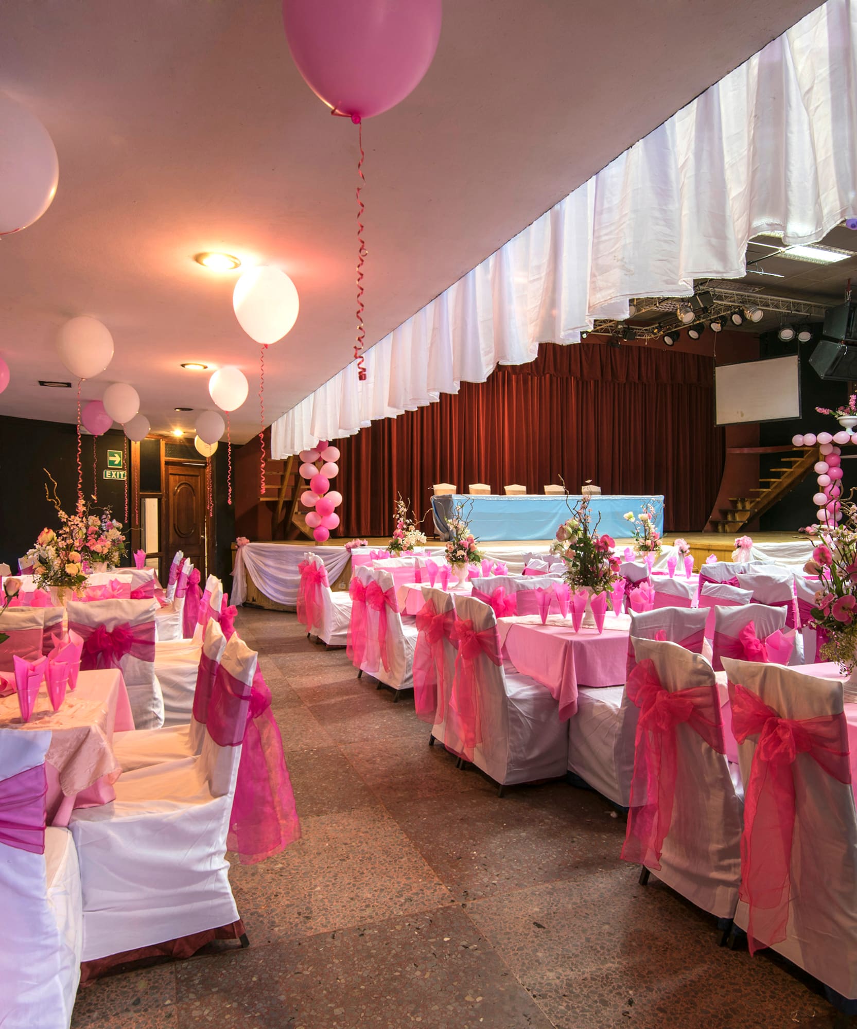 a room with tables and chairs with pink bows and balloons