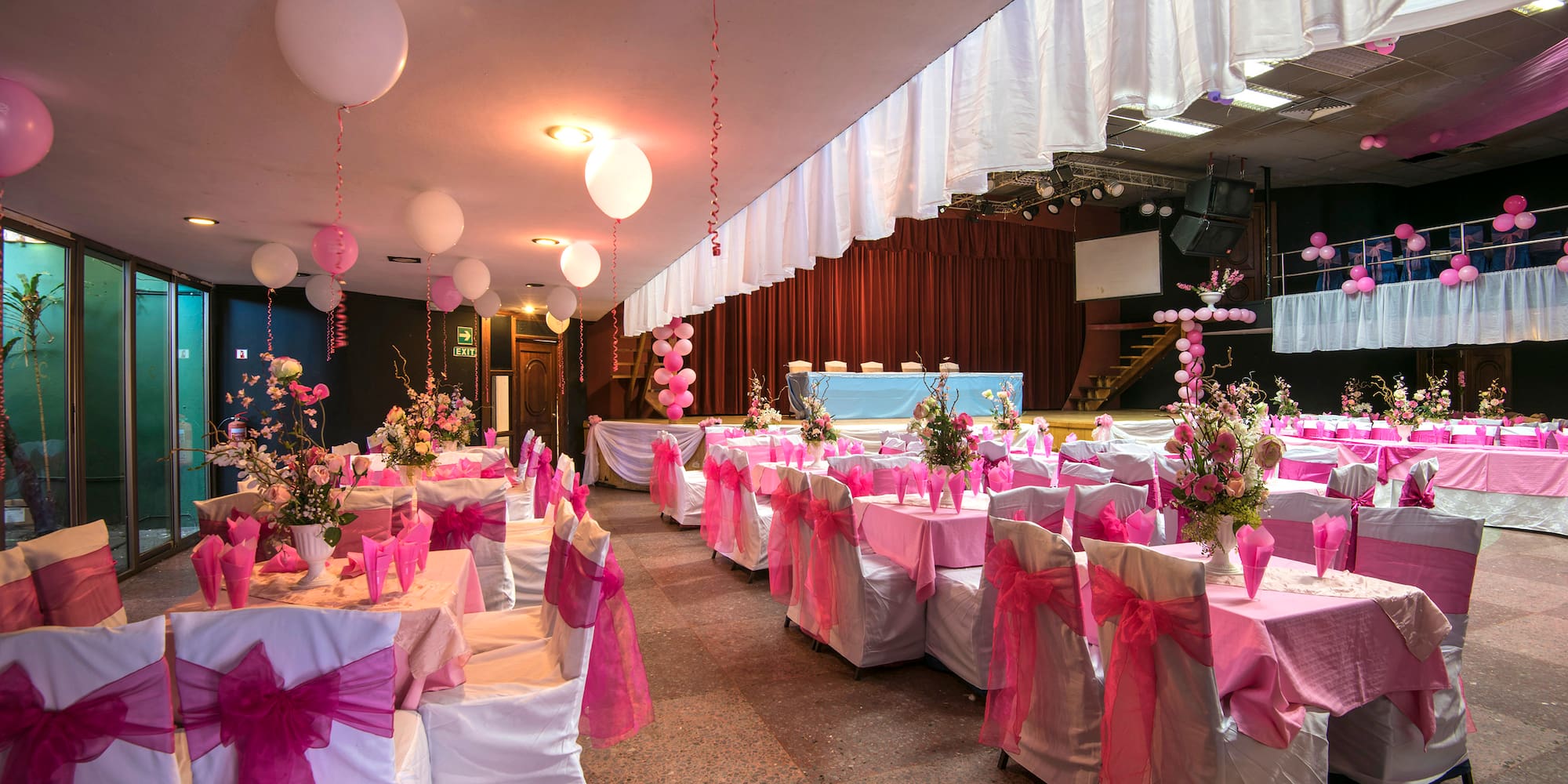 a room with tables and chairs with pink bows and balloons