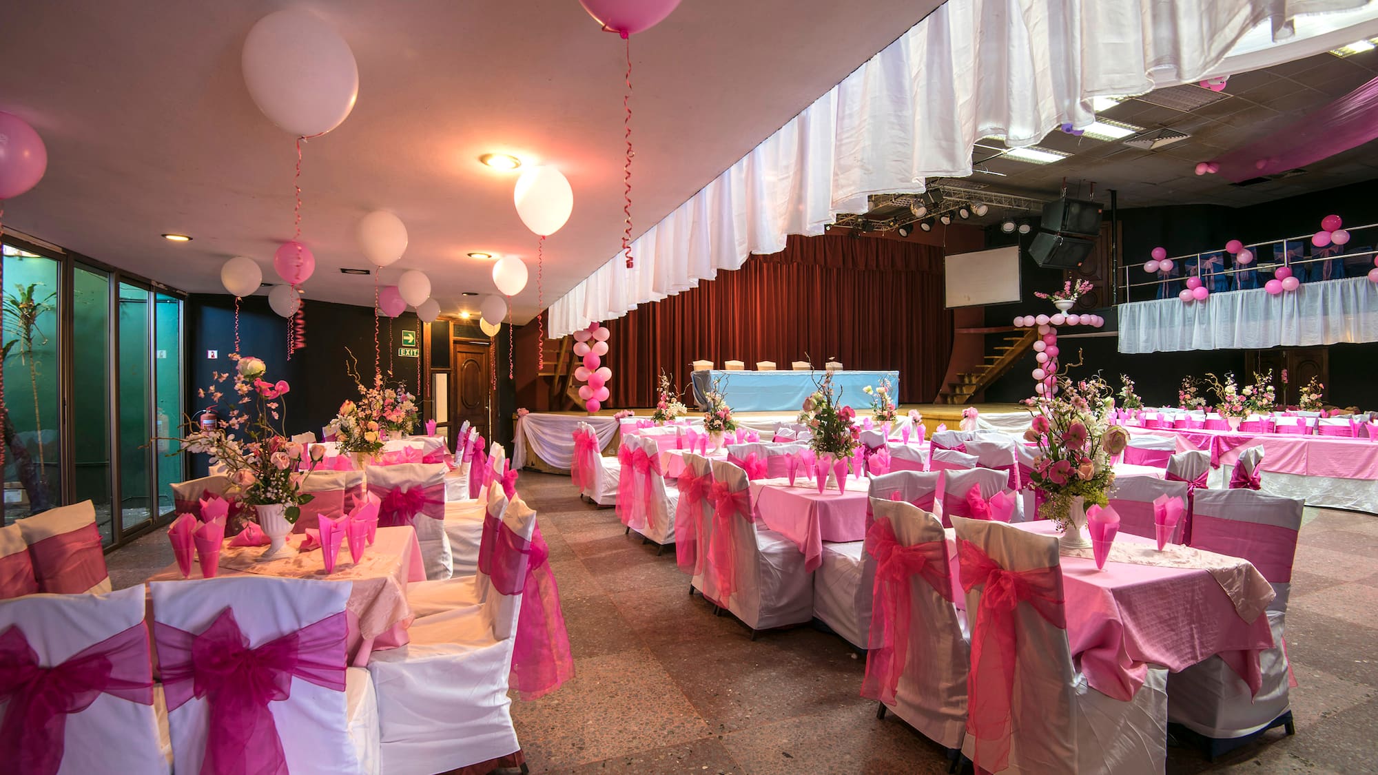 a room with tables and chairs with pink bows and balloons