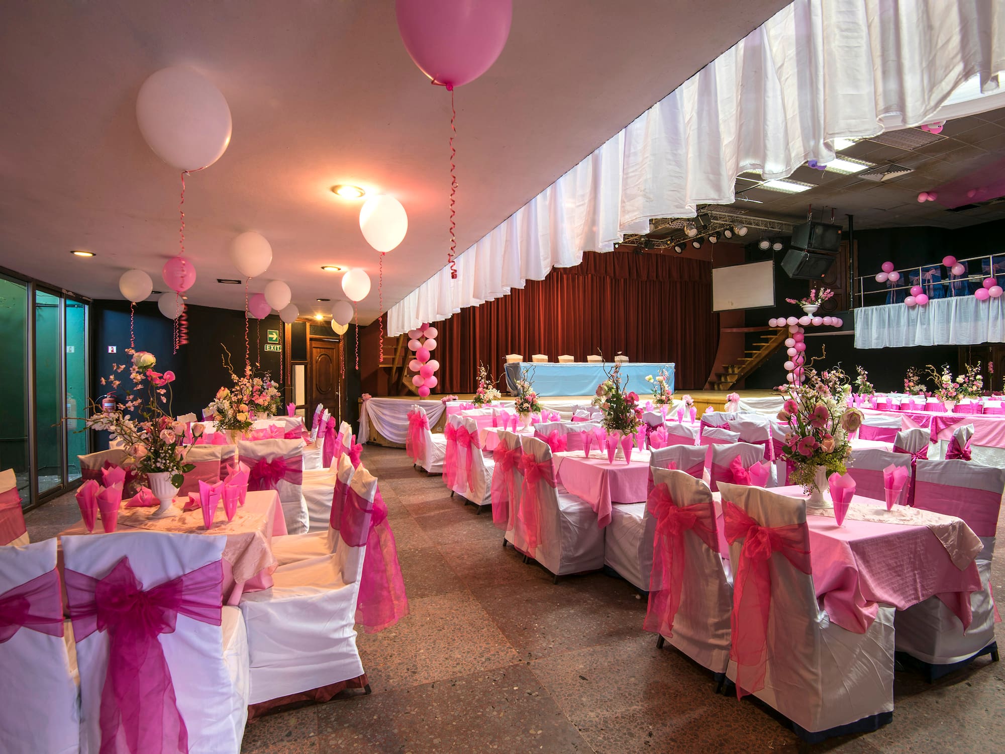 a room with tables and chairs with pink bows and balloons