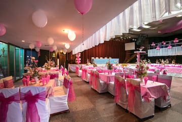 a room with tables and chairs with pink bows and balloons