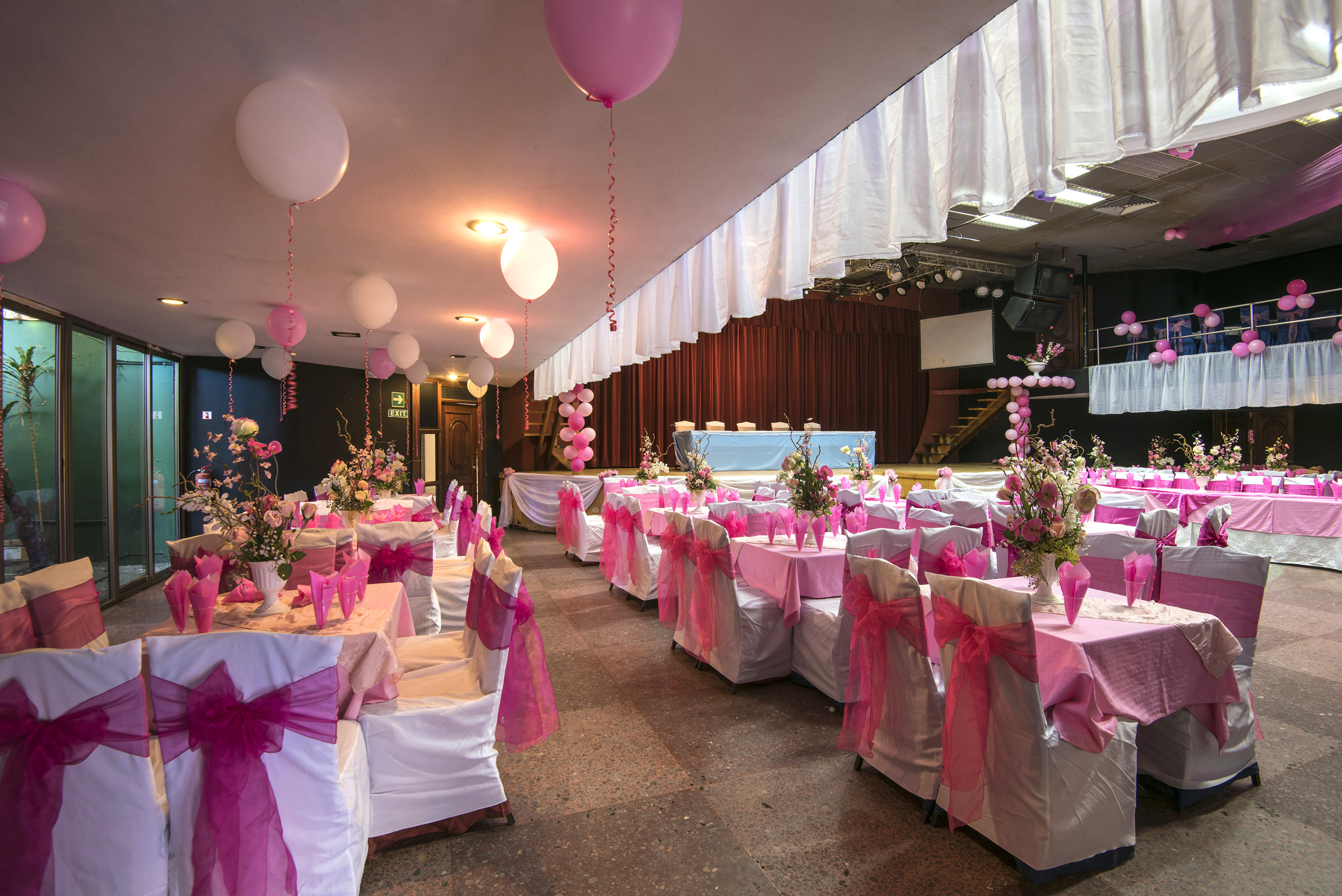 a room with tables and chairs with pink bows and balloons