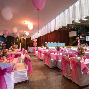a room with tables and chairs with pink bows and balloons
