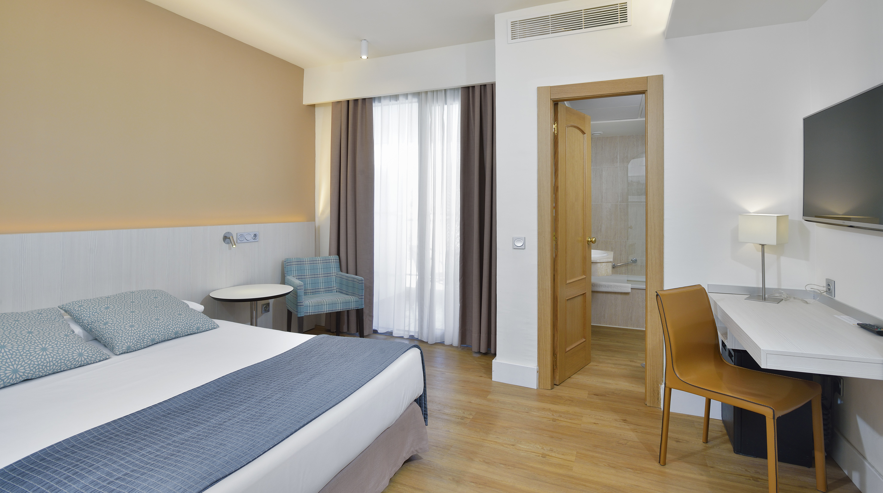 Modern hotel room with bed, desk, TV, and open door to bathroom.