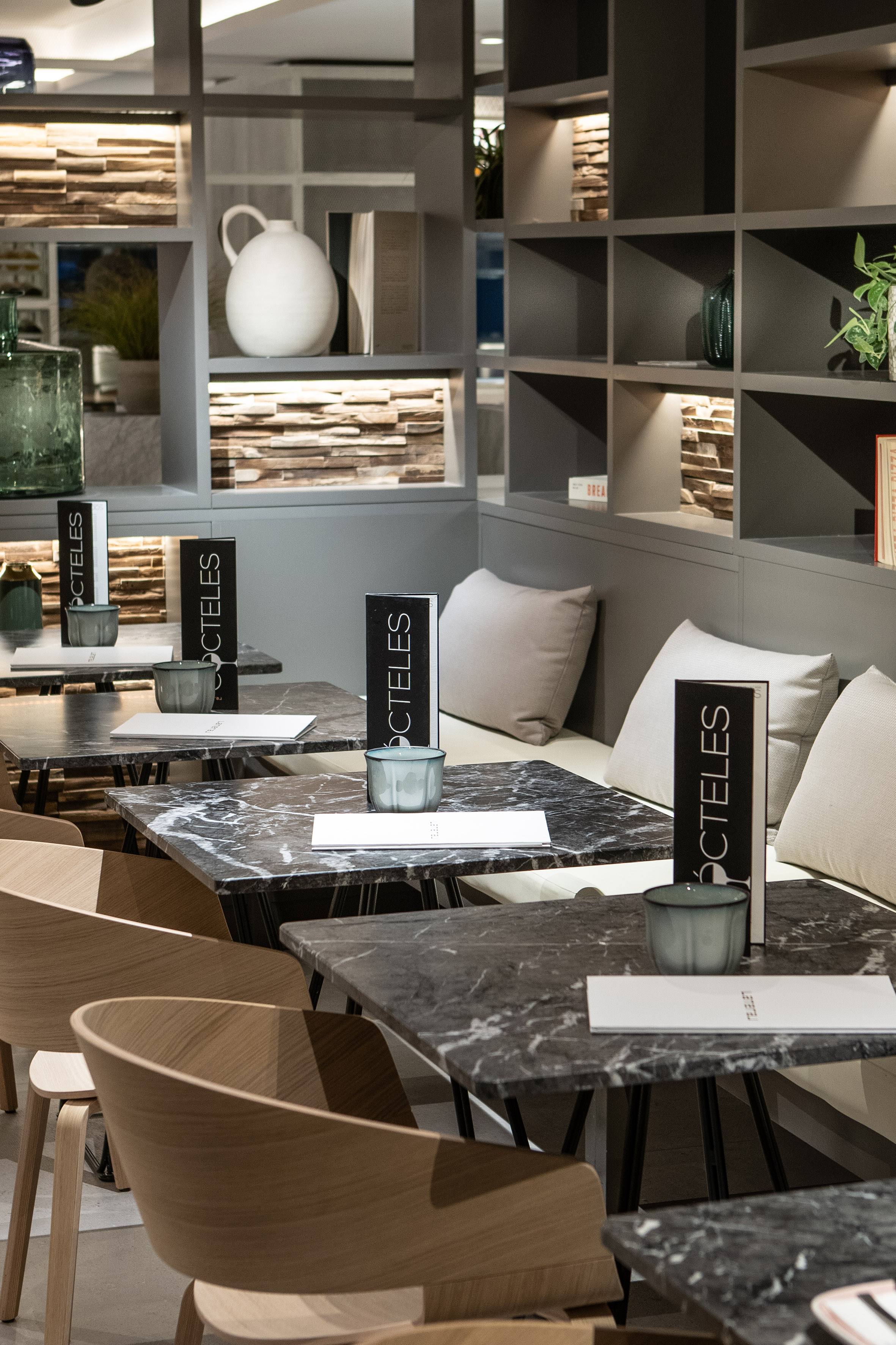 Modern bar interior with marble tables, wooden chairs, and cocktail menus.