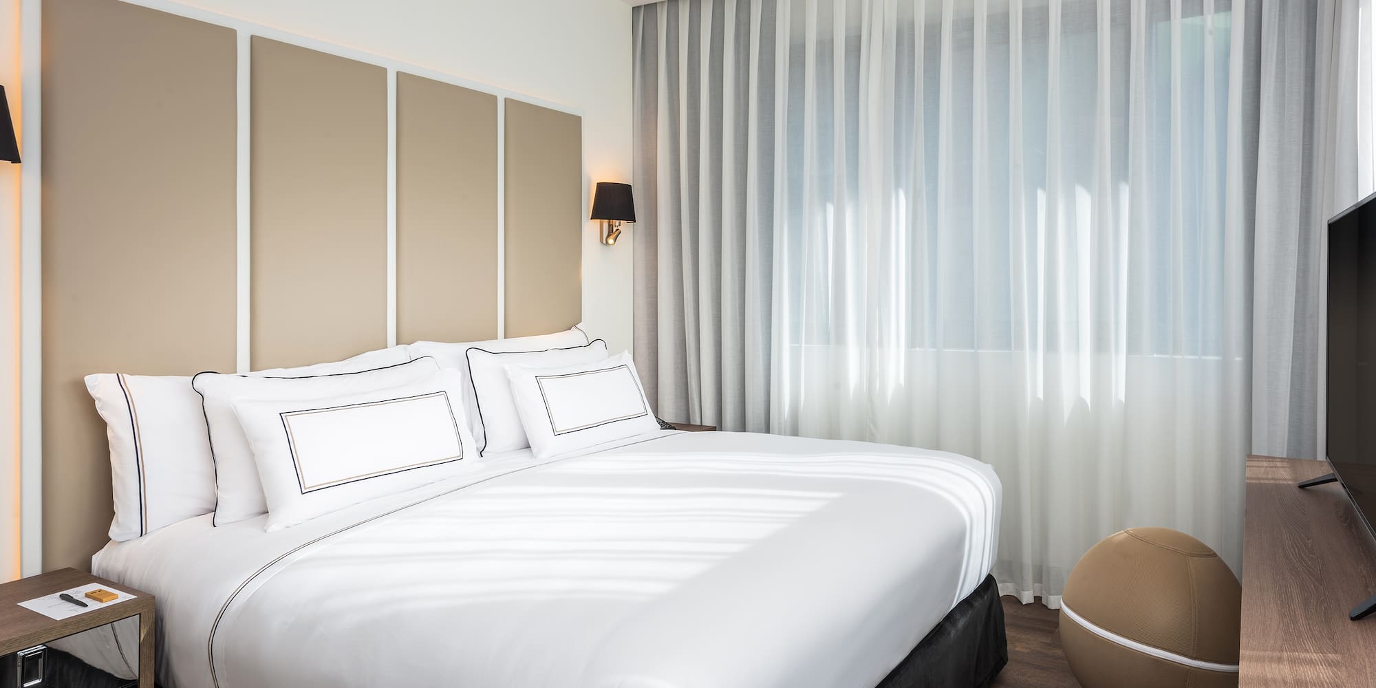 a bed with white sheets and a brown ball in front of it