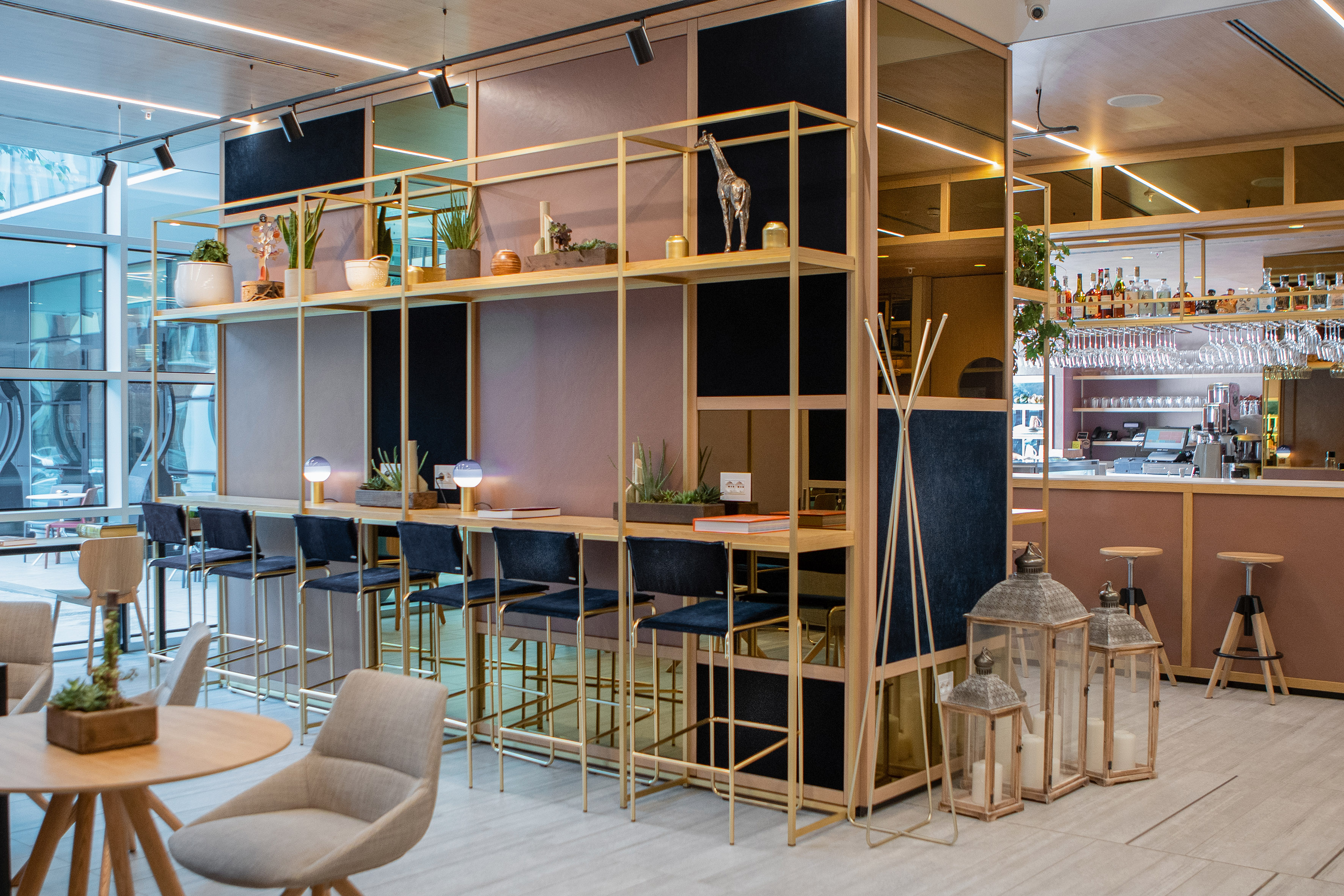 Modern hotel bar lounge with gold shelving, communal table, and lounge seats.