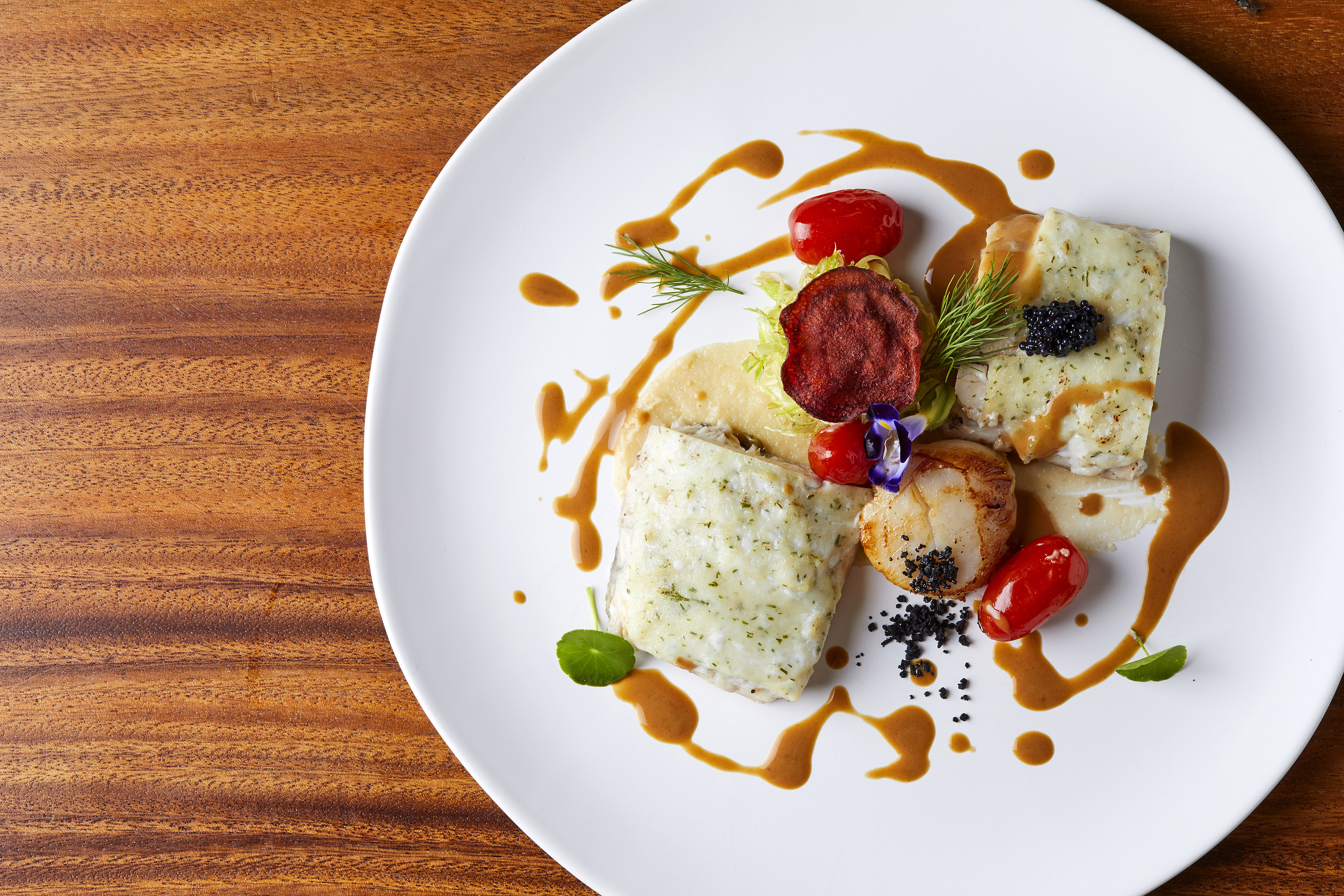 Gourmet fish fillets and scallops with caviar, tomatoes, and sauce.