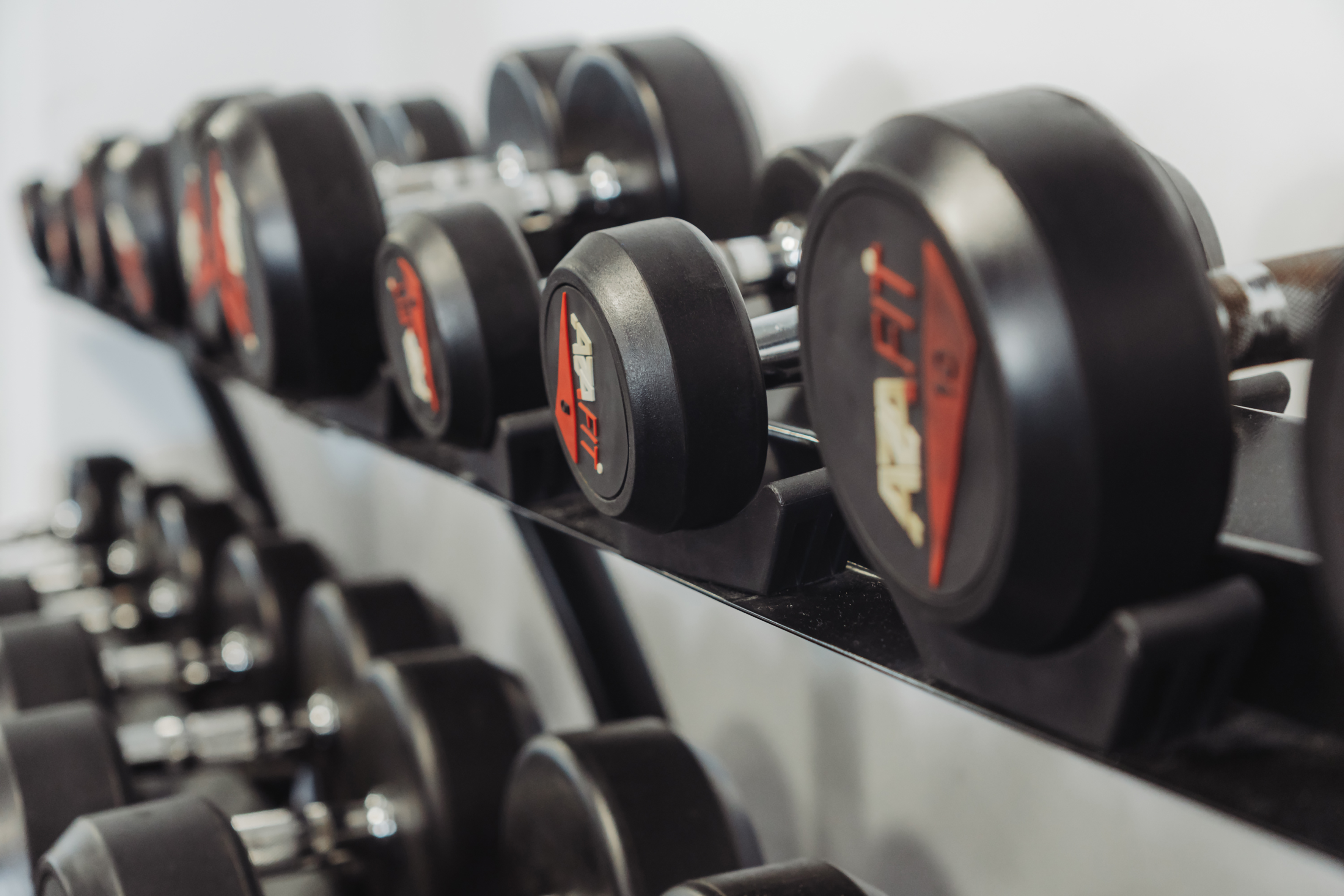 Black AZA FIT dumbbells on a gym rack for fitness and strength training.