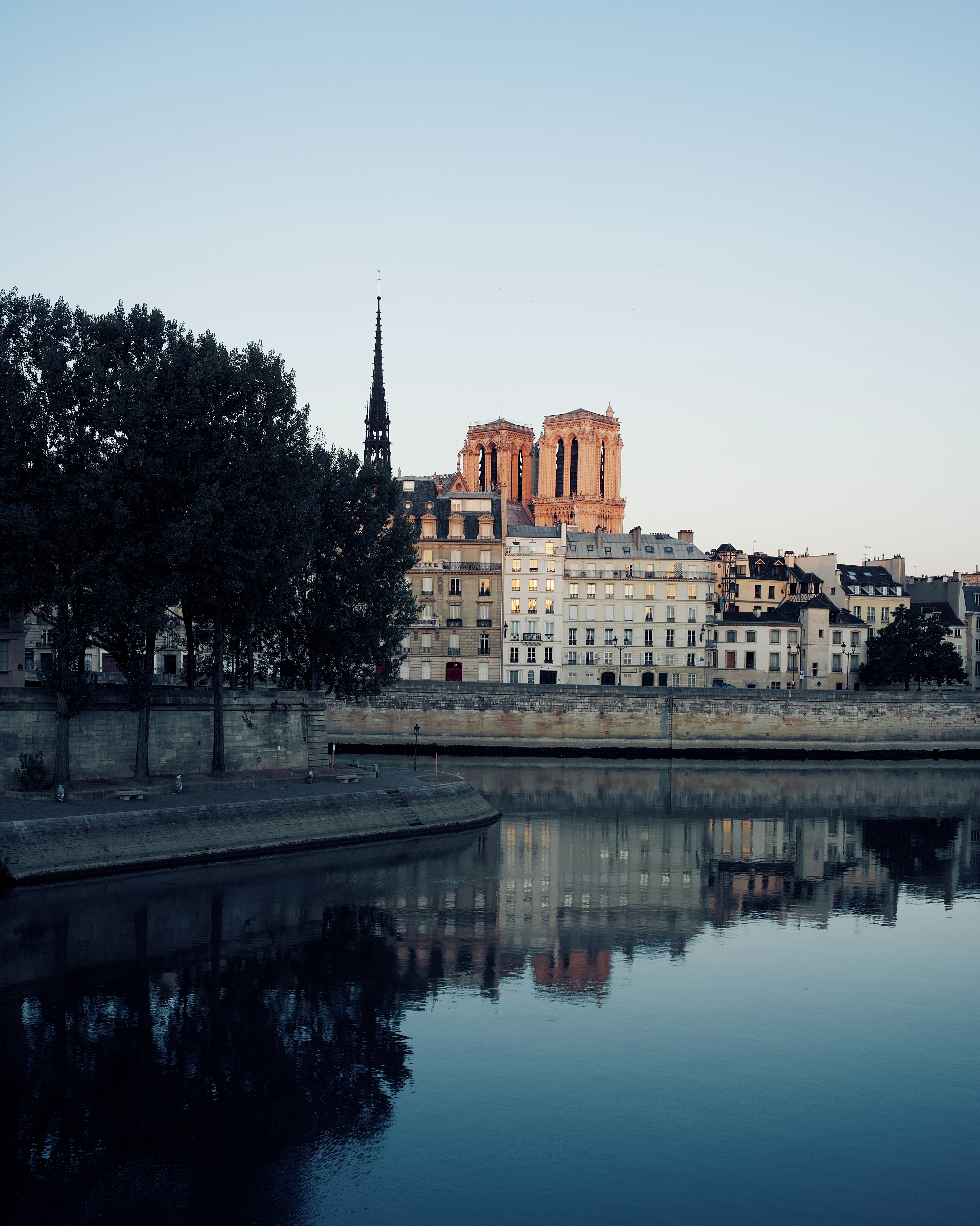 Notre Dame Cathedral and Parisian buildings reflected in Seine River at dawn.