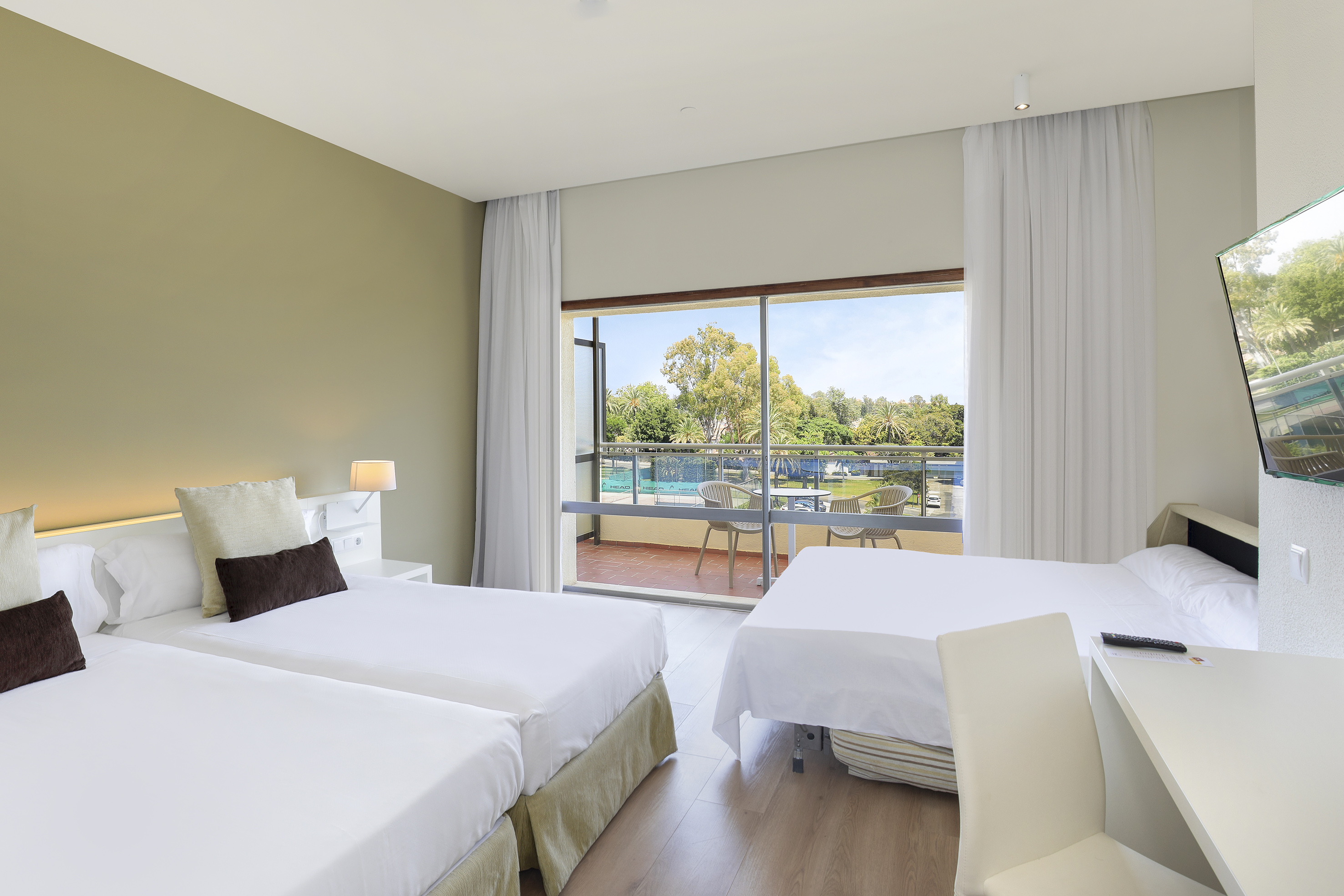 Bright hotel room with three beds, private balcony, and resort pool view.