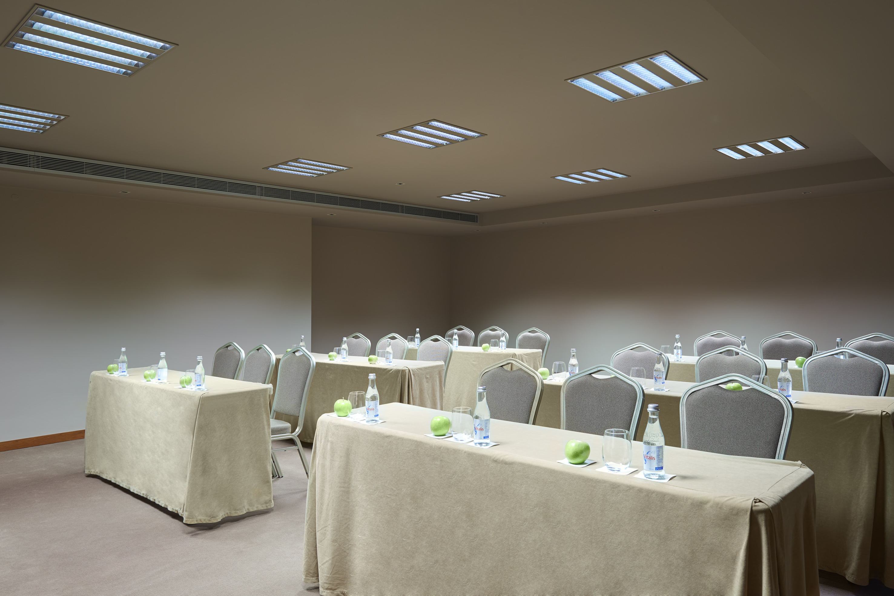 Conference room setup with tables, chairs, water bottles, and green apples.