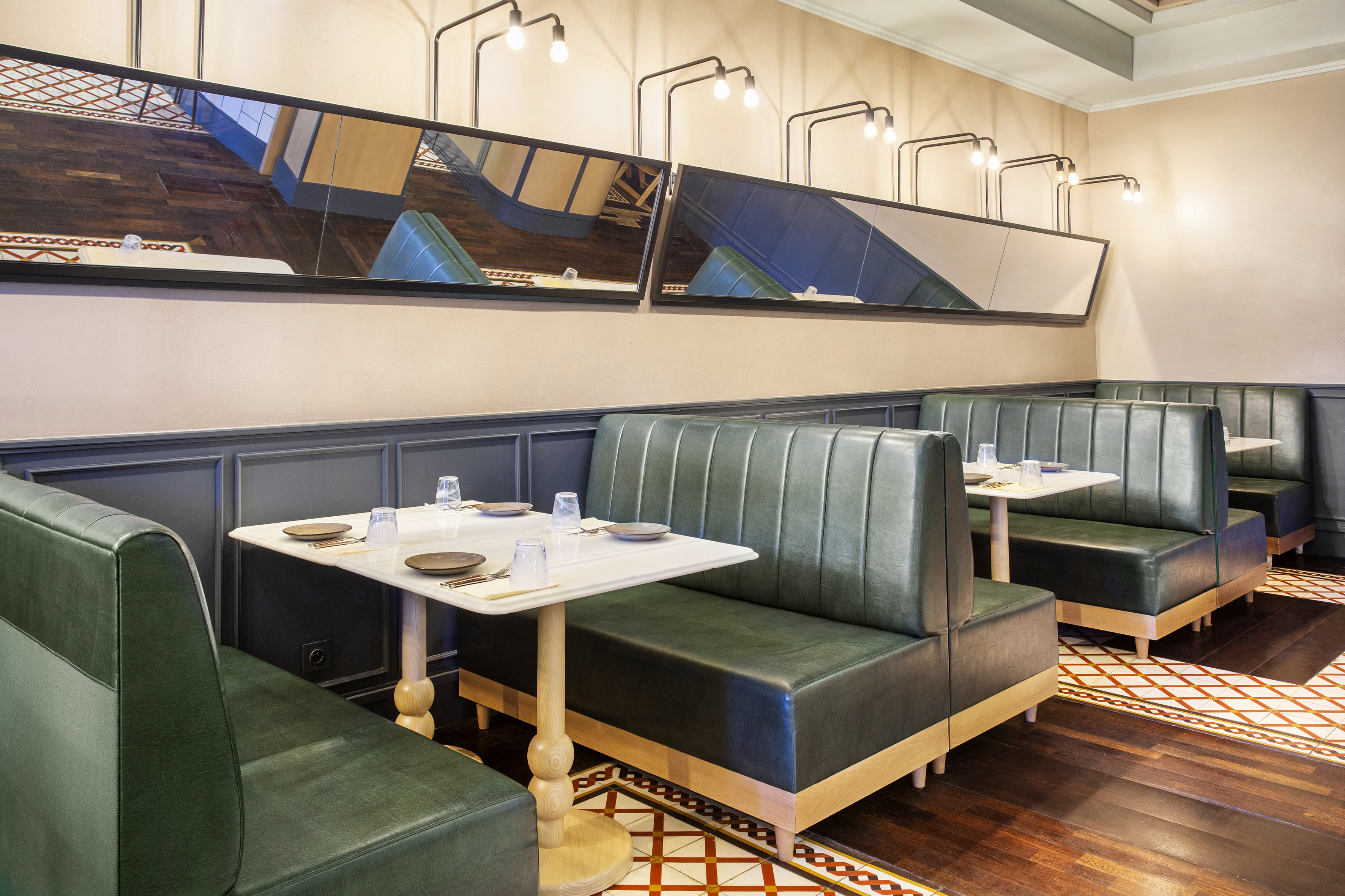 Modern restaurant interior with green leather booths, marble tables, tiled floor.