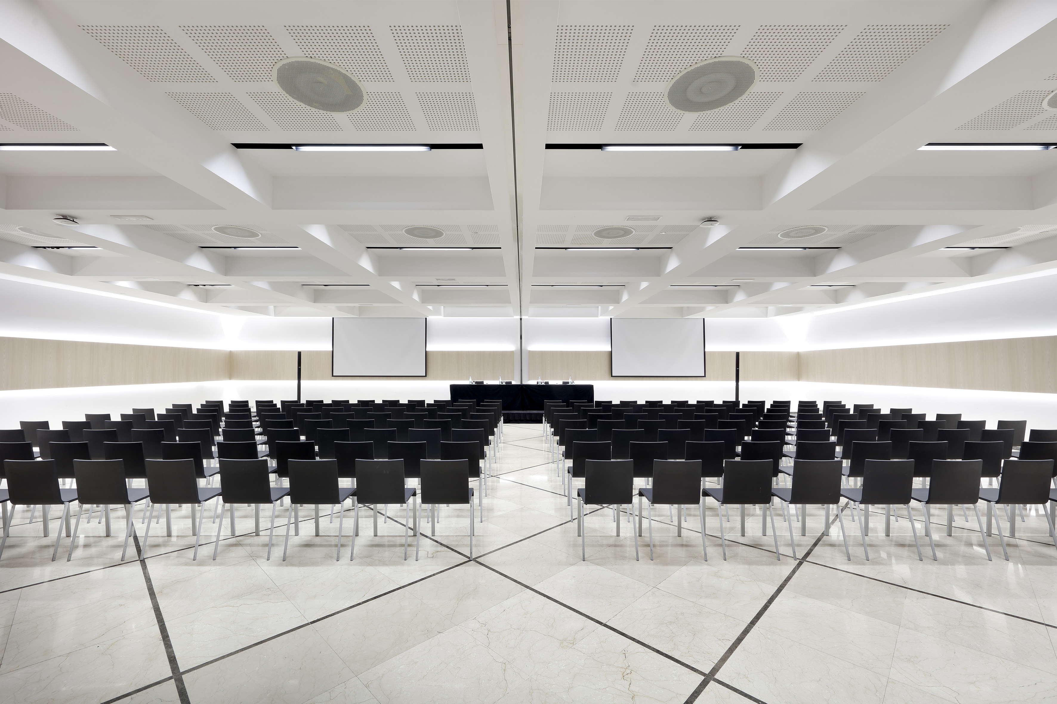 Modern conference room with rows of chairs, dual screens, and a speaker table.