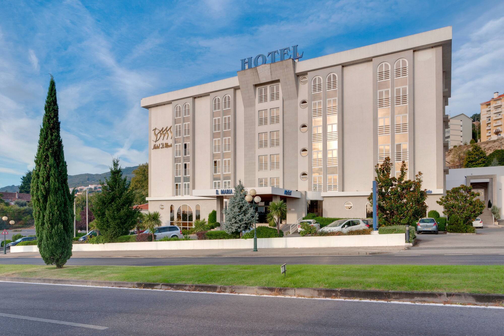 Modern Hotel D. Maria building exterior with tall trees and road.