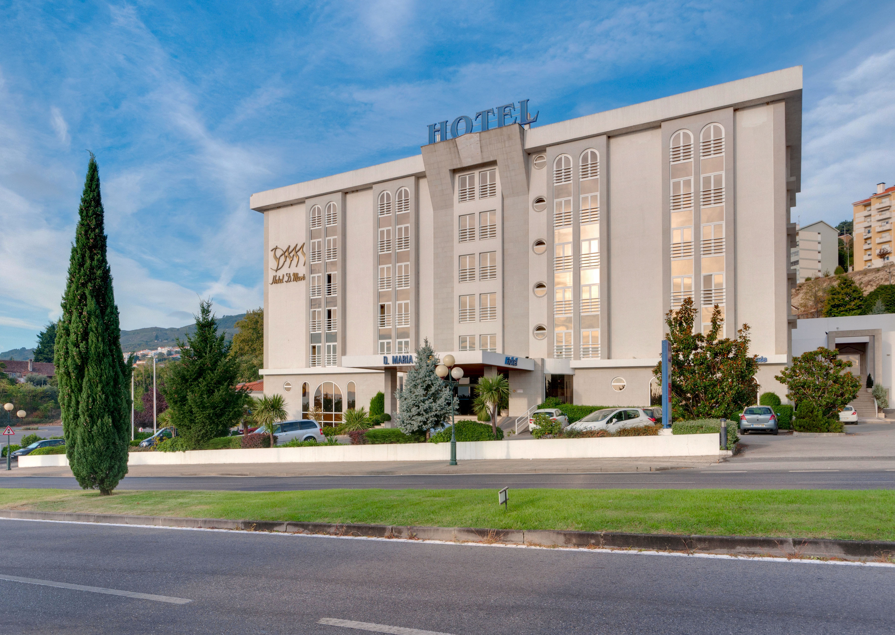 Modern Hotel D. Maria building exterior with tall trees and road.