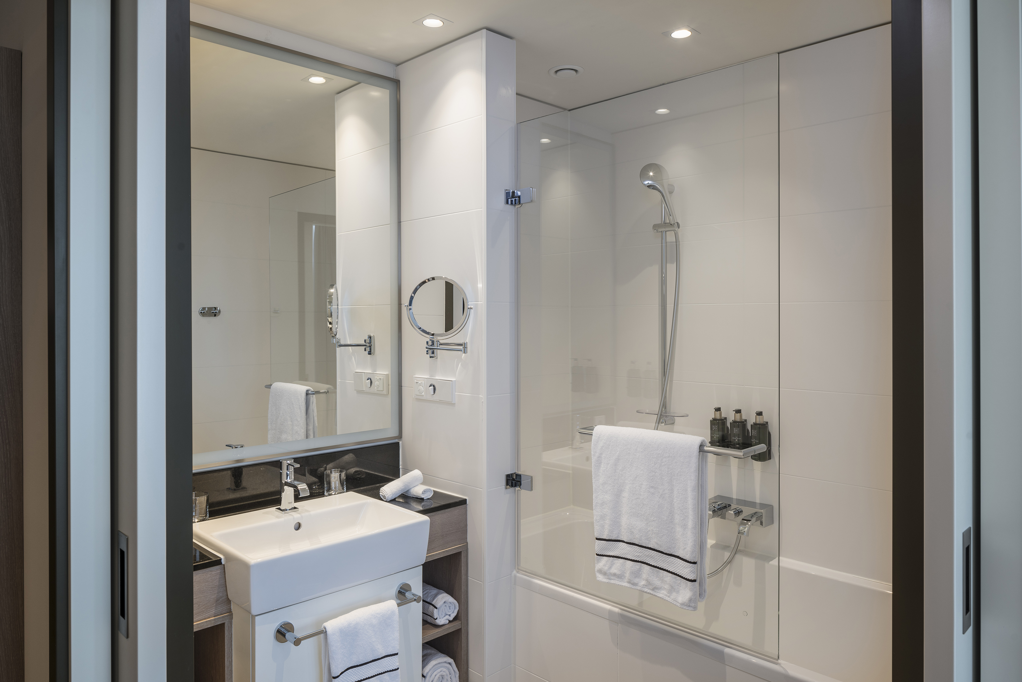 Modern white bathroom with vanity, large mirror, and shower-bathtub combo.