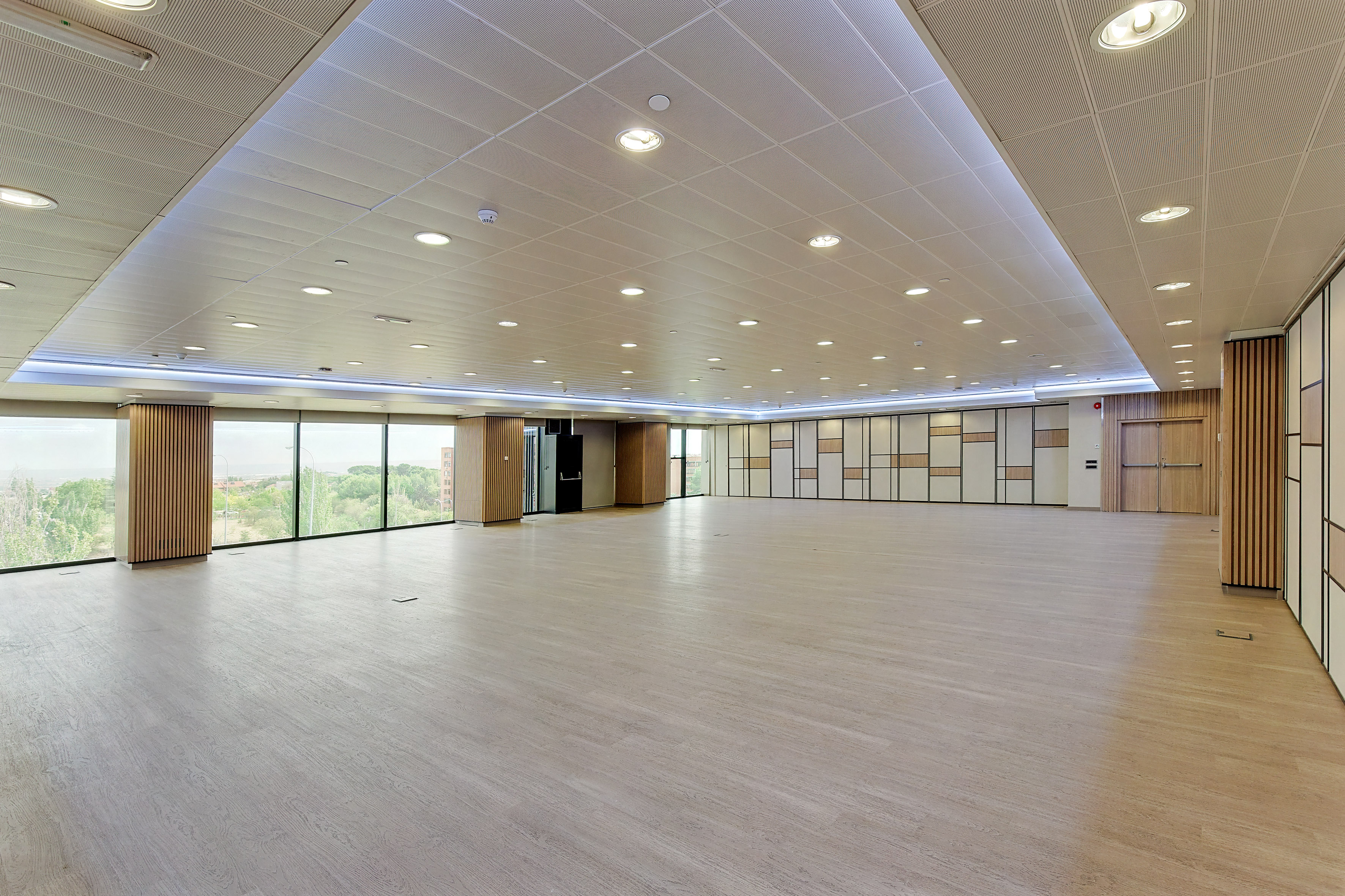 Spacious modern event hall with large windows, wooden floor, and contemporary design.