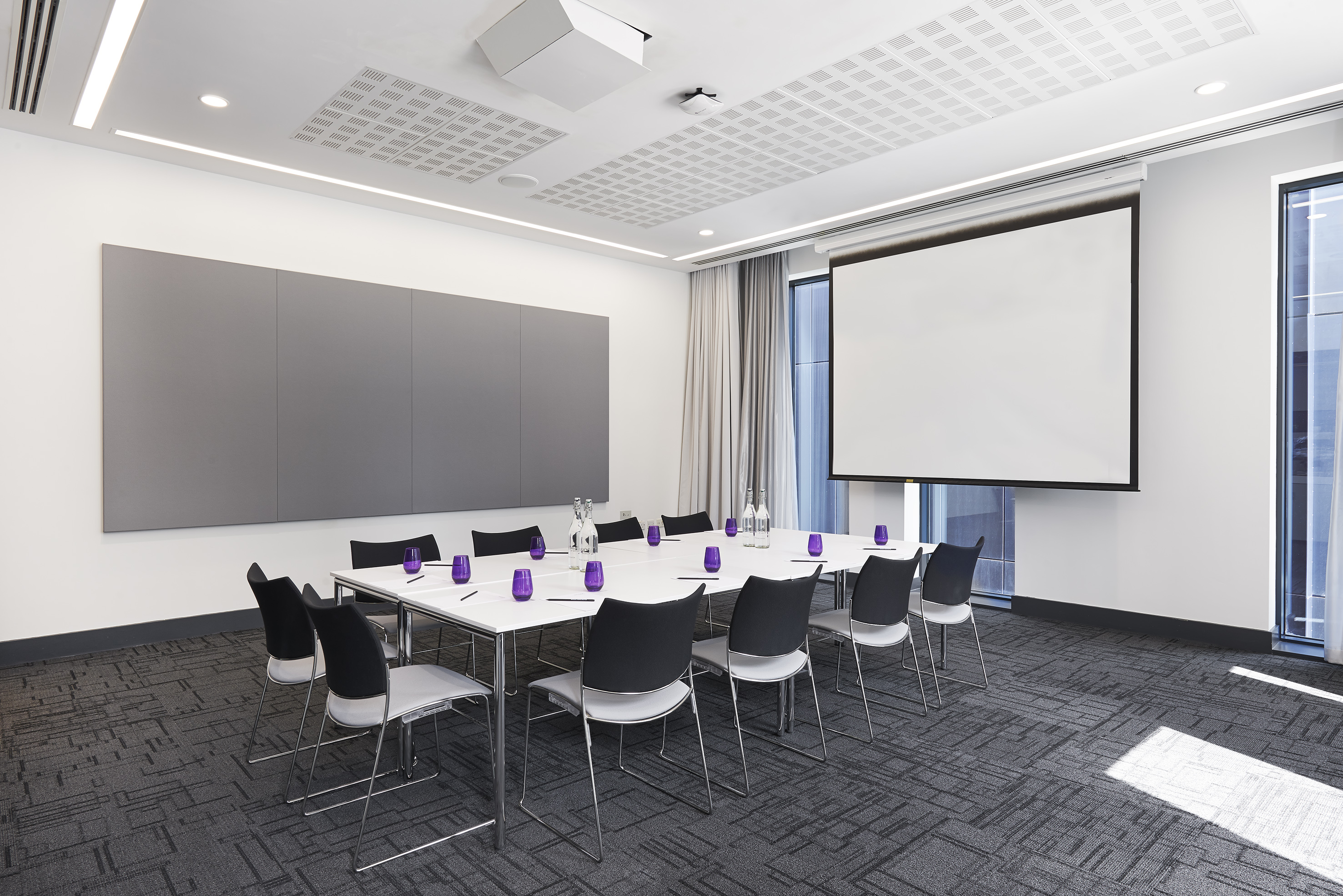 Modern meeting room with projection screen, conference table, and chairs.