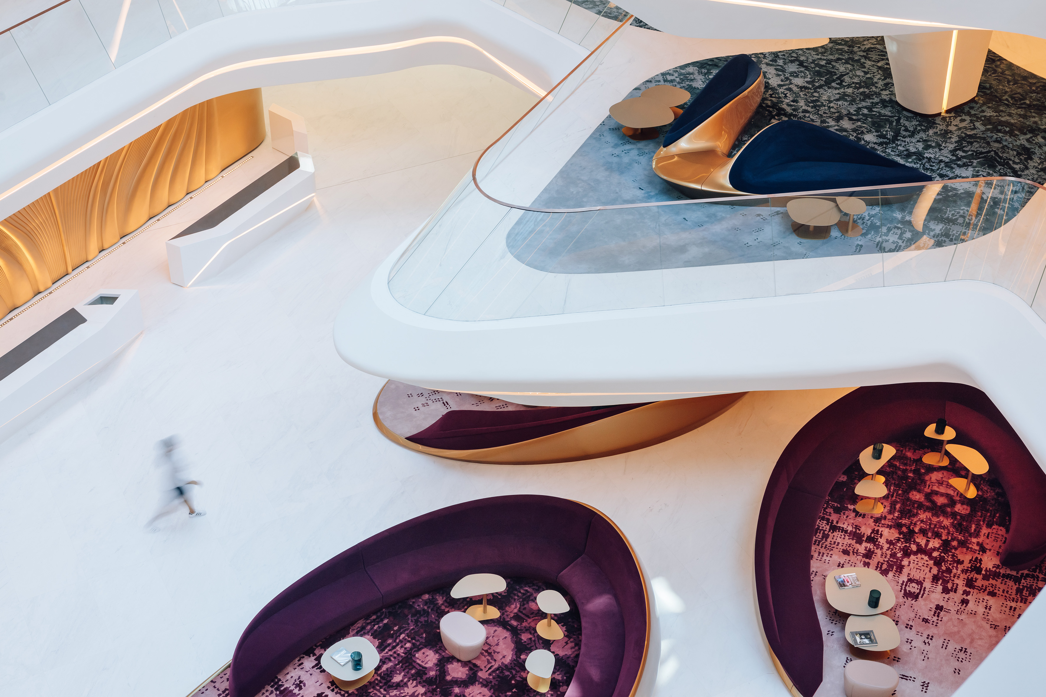 Modern architectural lounge with curved purple and blue sofas, gold accents.