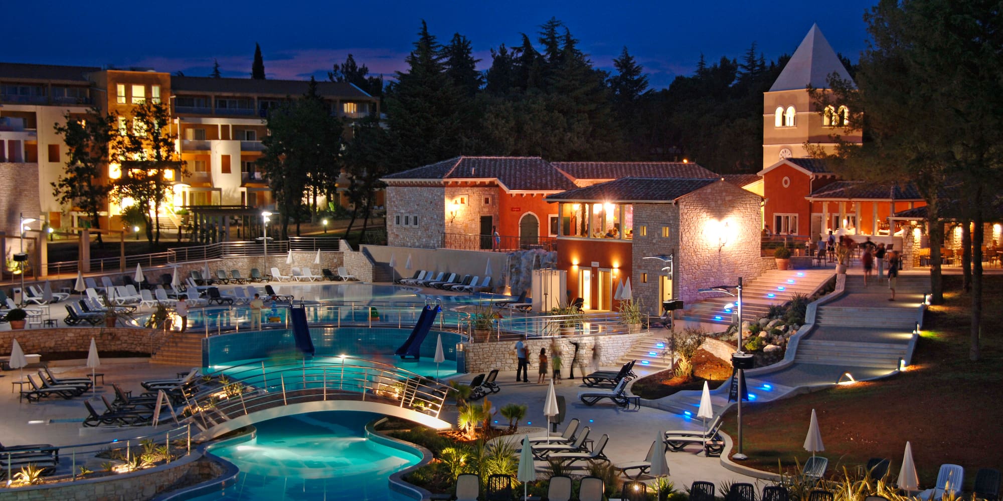 a pool with a bridge and chairs in front of buildings