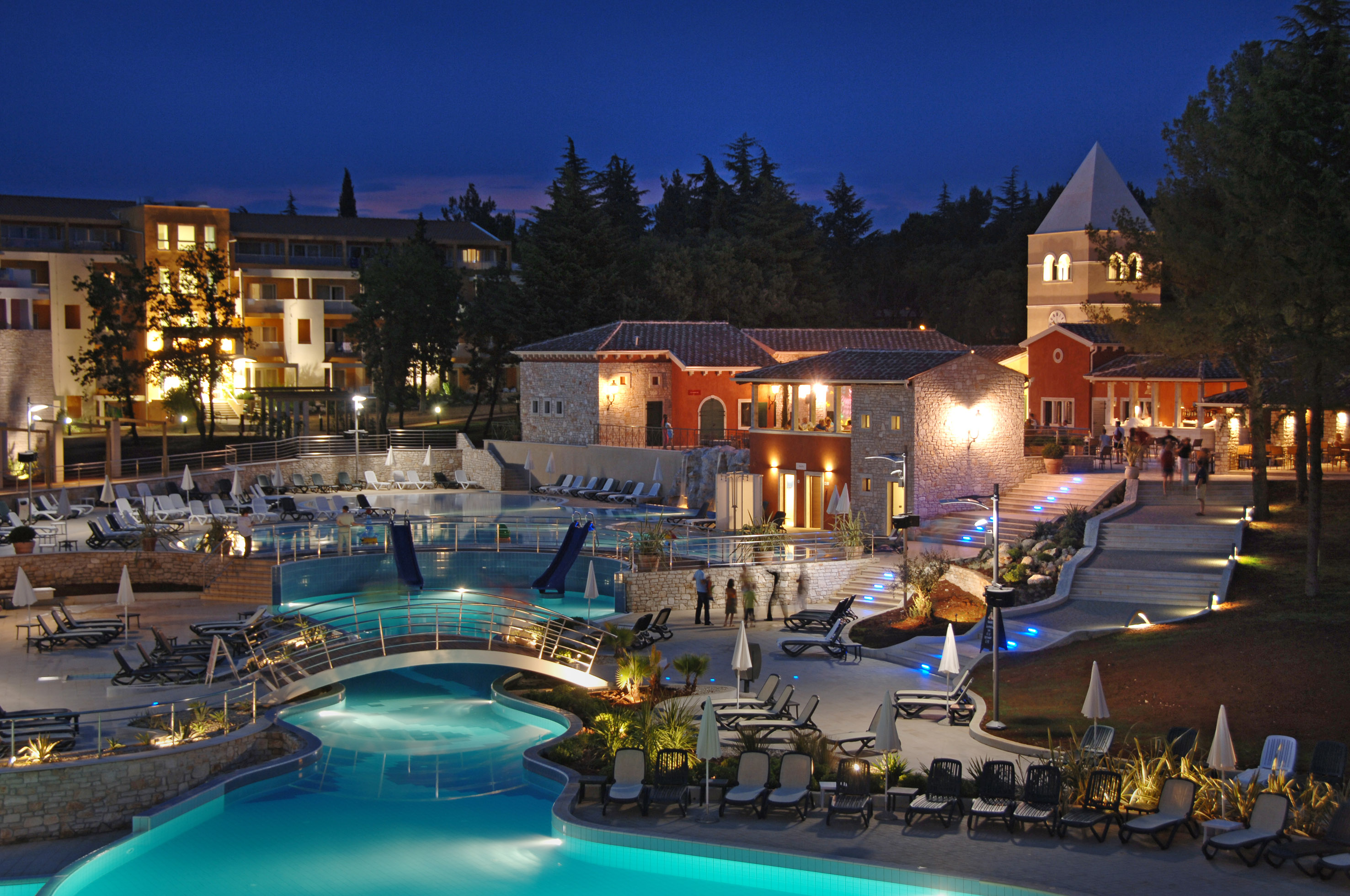 a pool with a bridge and chairs in front of buildings