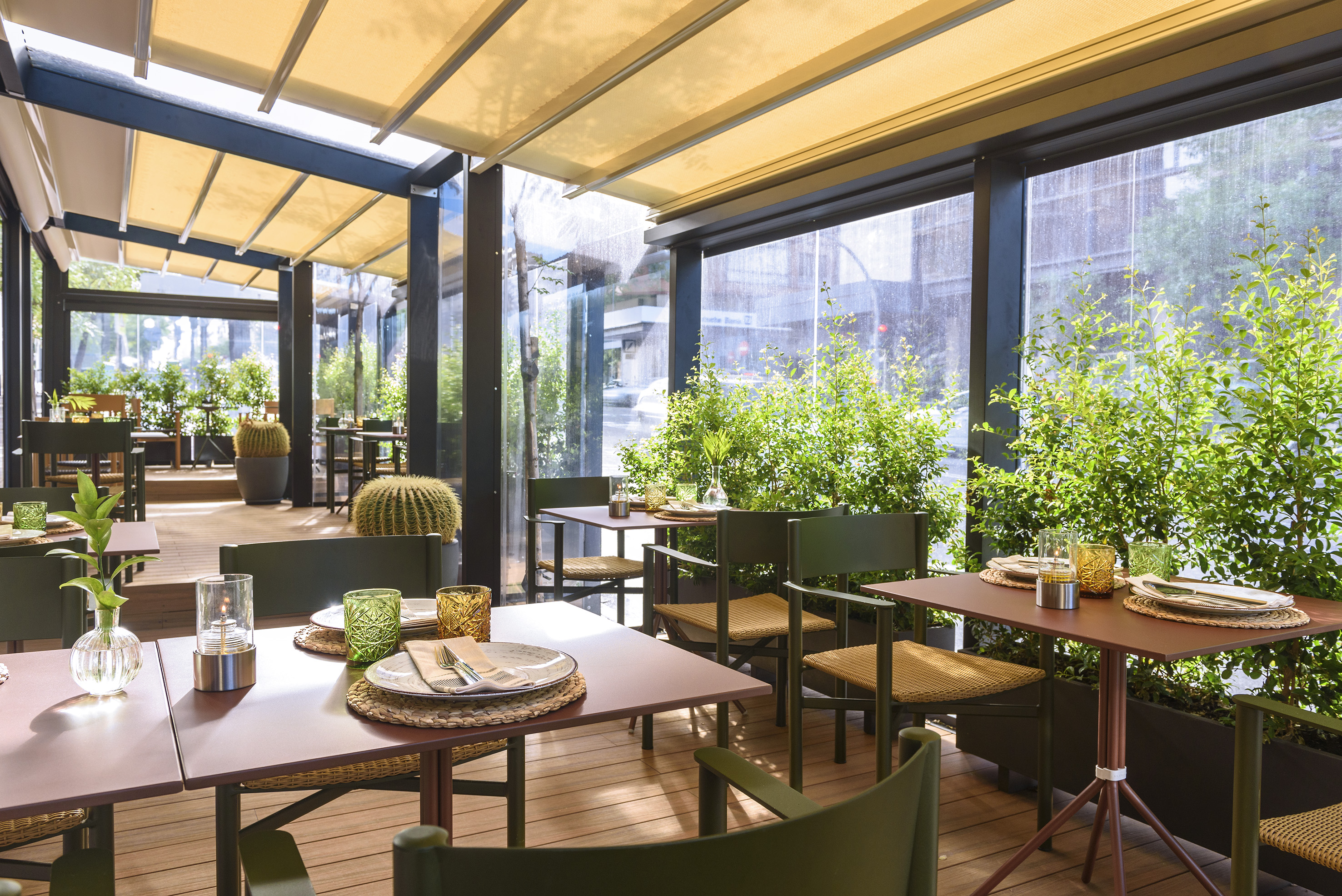 Stylish outdoor dining patio with green furniture, lush plants, and retractable awning.