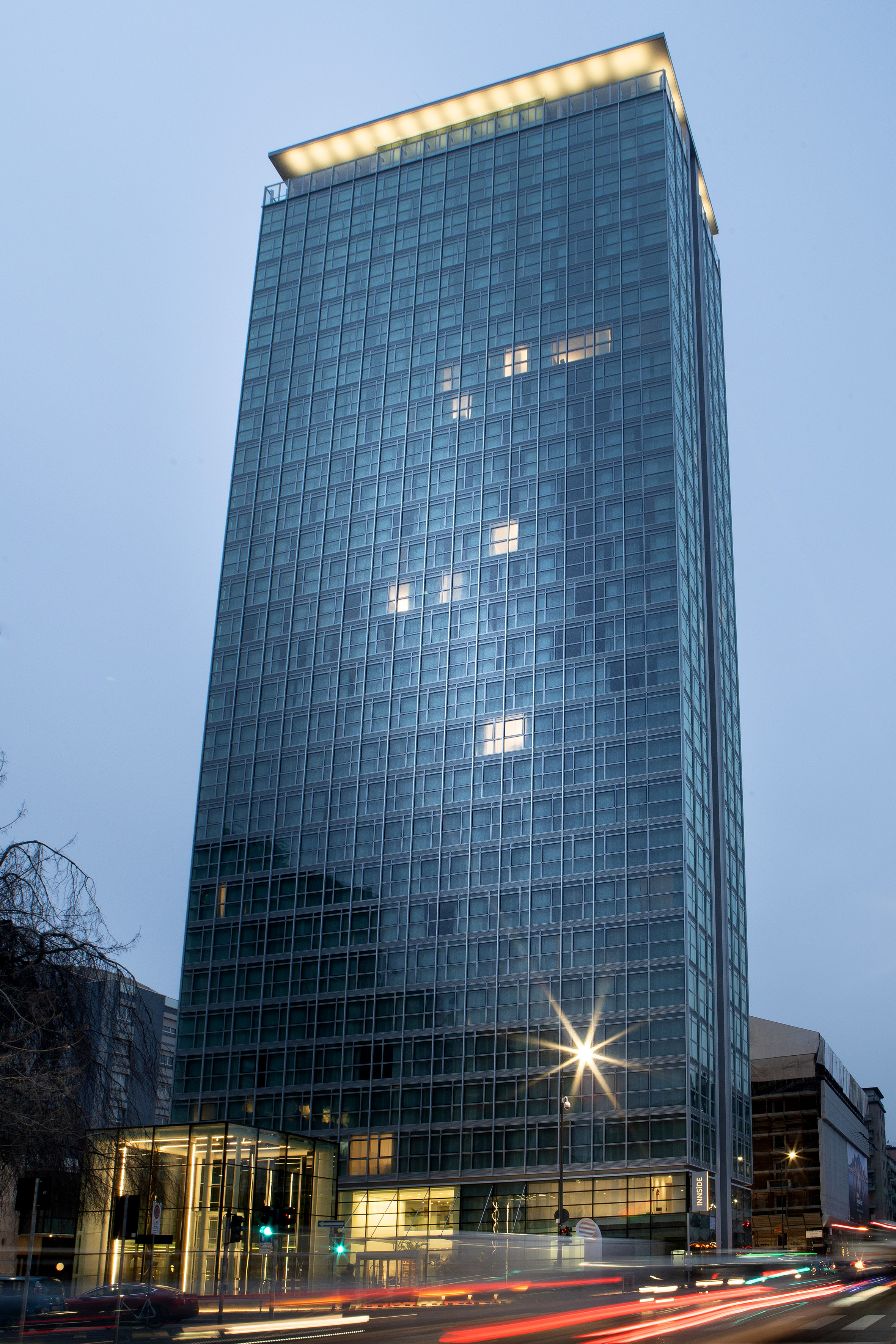 Modern glass skyscraper illuminated at dusk with light trails from city traffic.